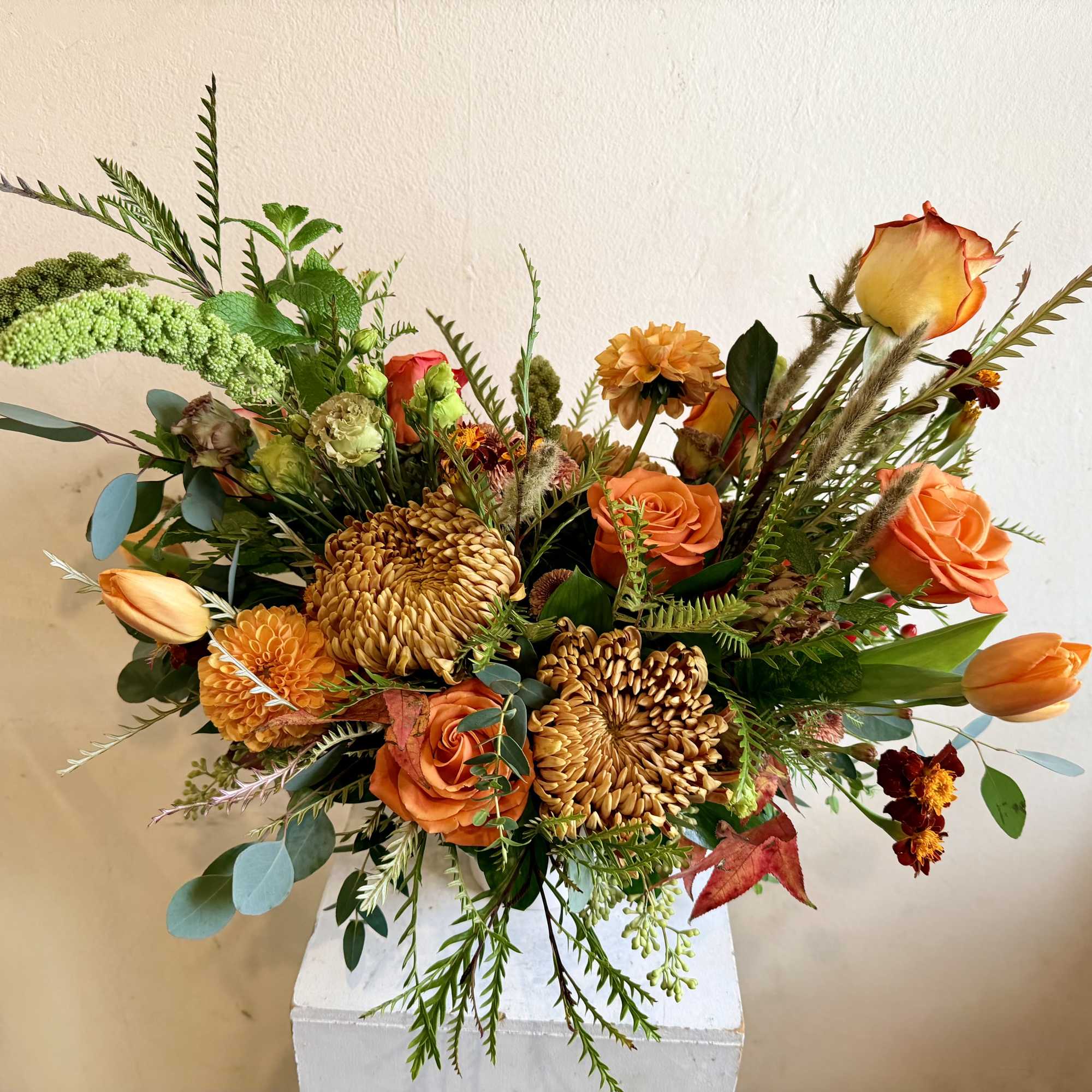 Orange and gold floral arrangement with roses and chrysanthemums in a white vase