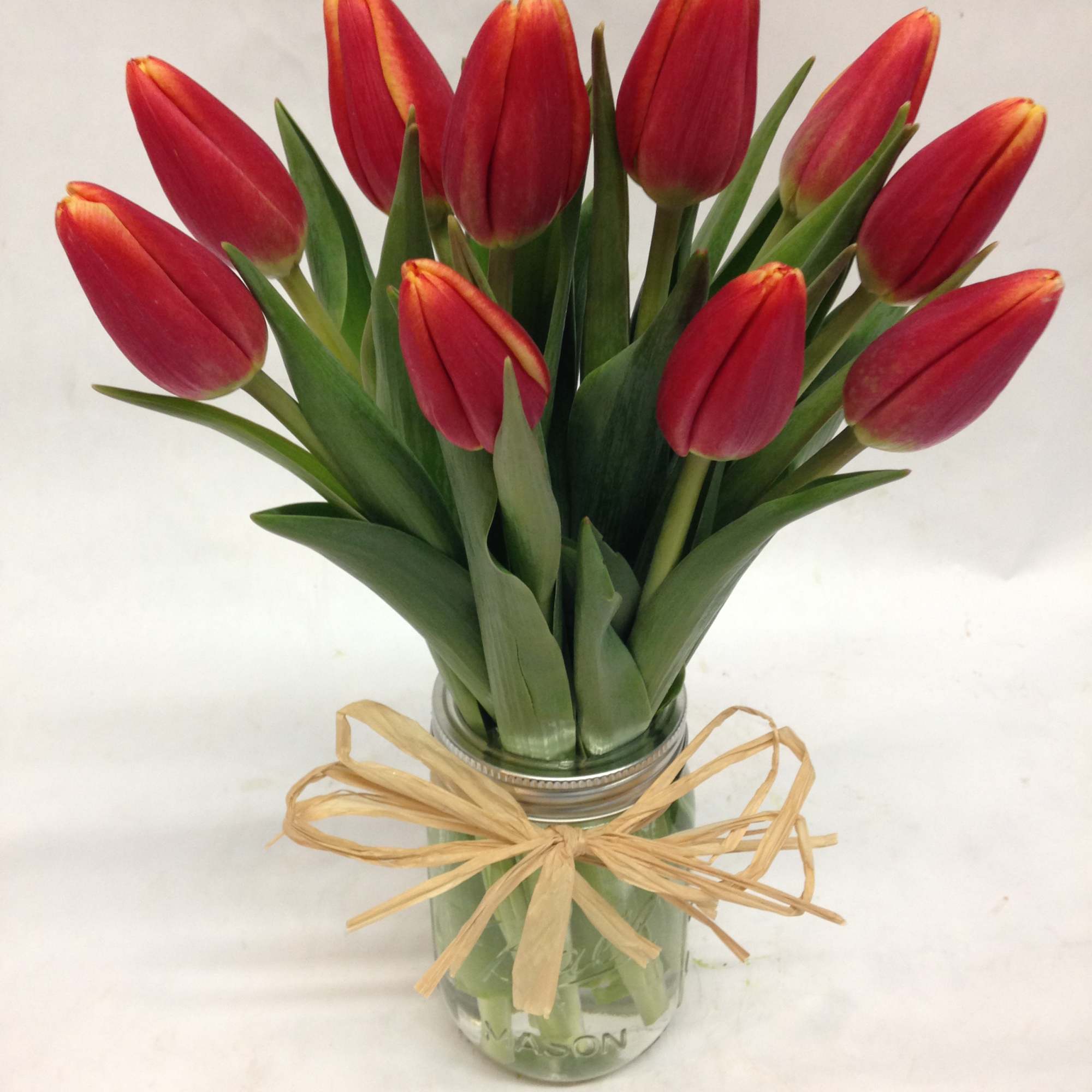 Red tulips in a glass jar tied with a raffia bow