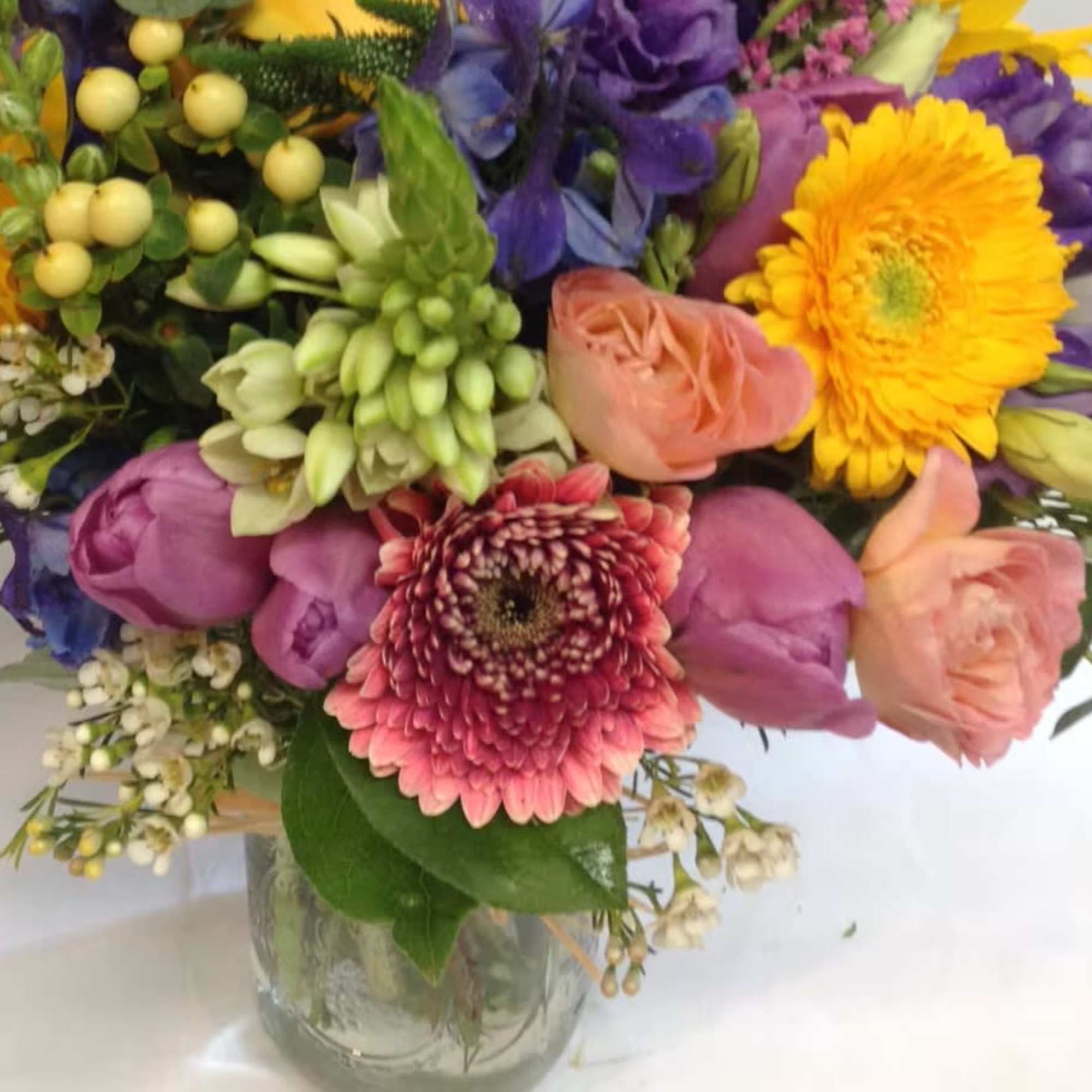 Mixed bouquet with gerbera daisies, roses, and purple blooms in a glass vase