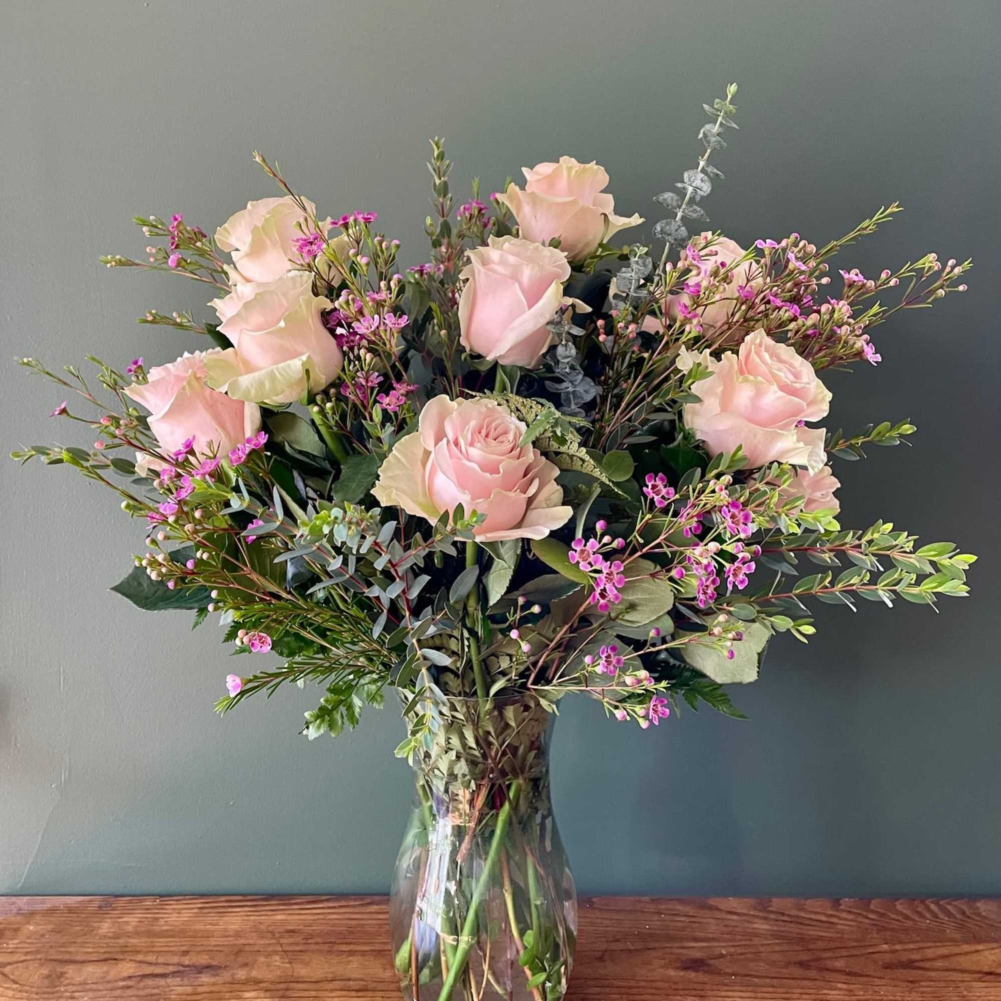 This classic arrangement features a dozen light pink roses accented with fresh
