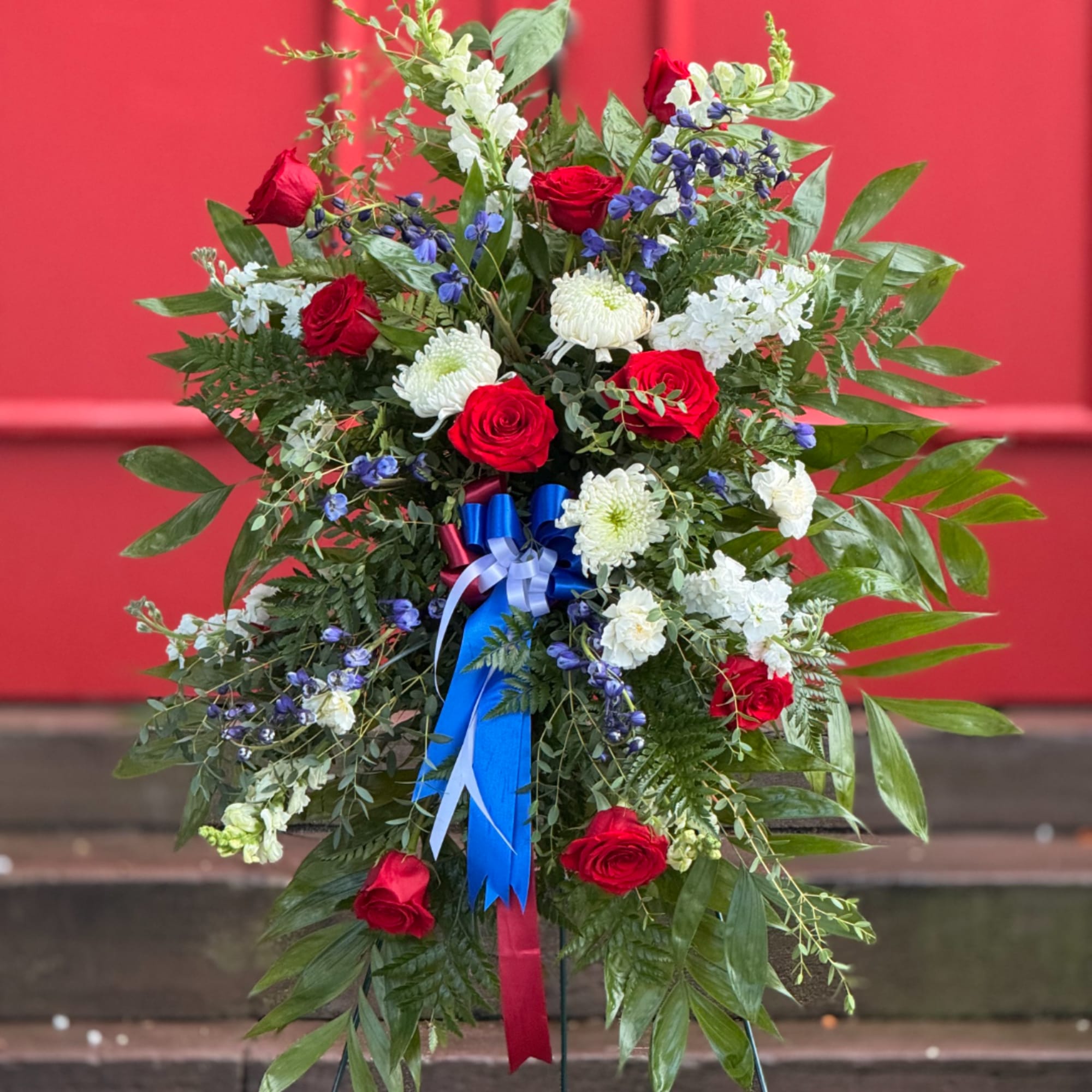 Standing floral spray with red roses, white mums, and blue ribbon accents
