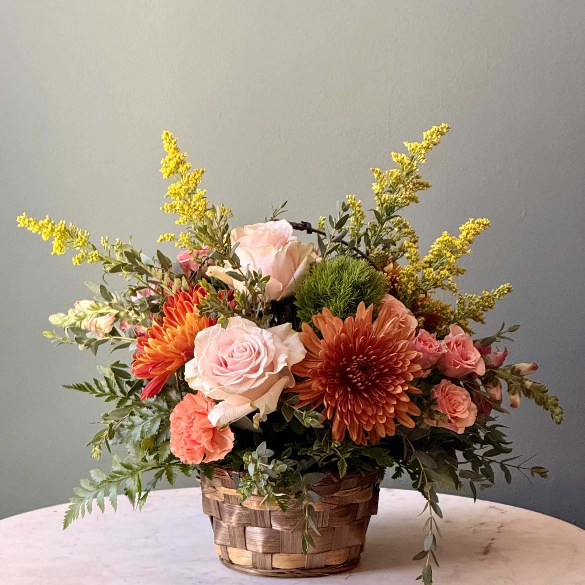 Basket arrangement with pink roses, orange chrysanthemums, and yellow filler flowers