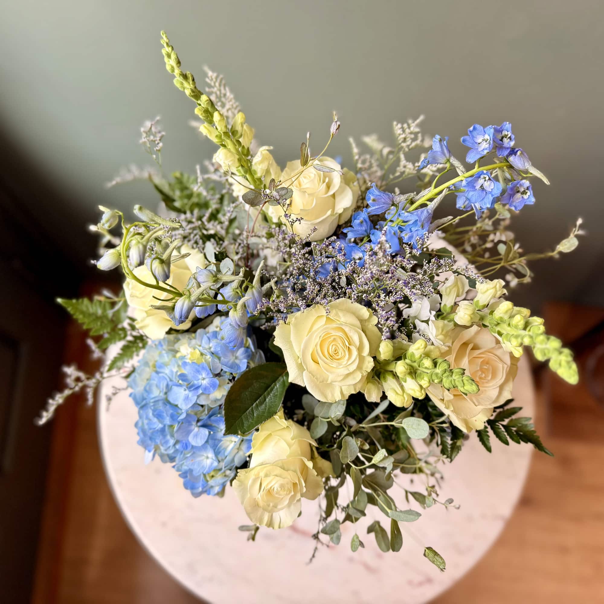 Top view of an arrangement with cream roses, blue hydrangeas, and blue delphinium.