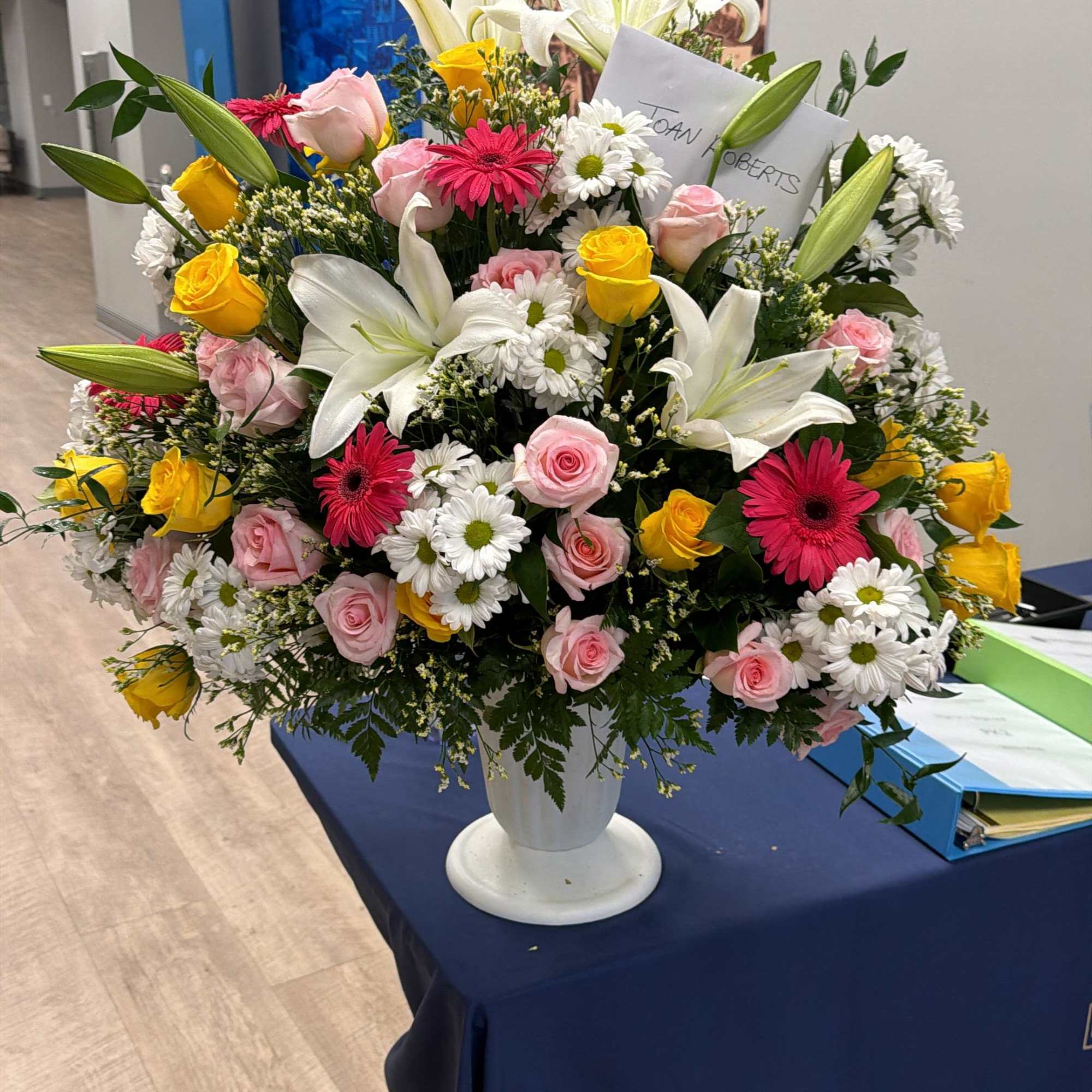 Large mixed flower arrangement in a white pedestal vase