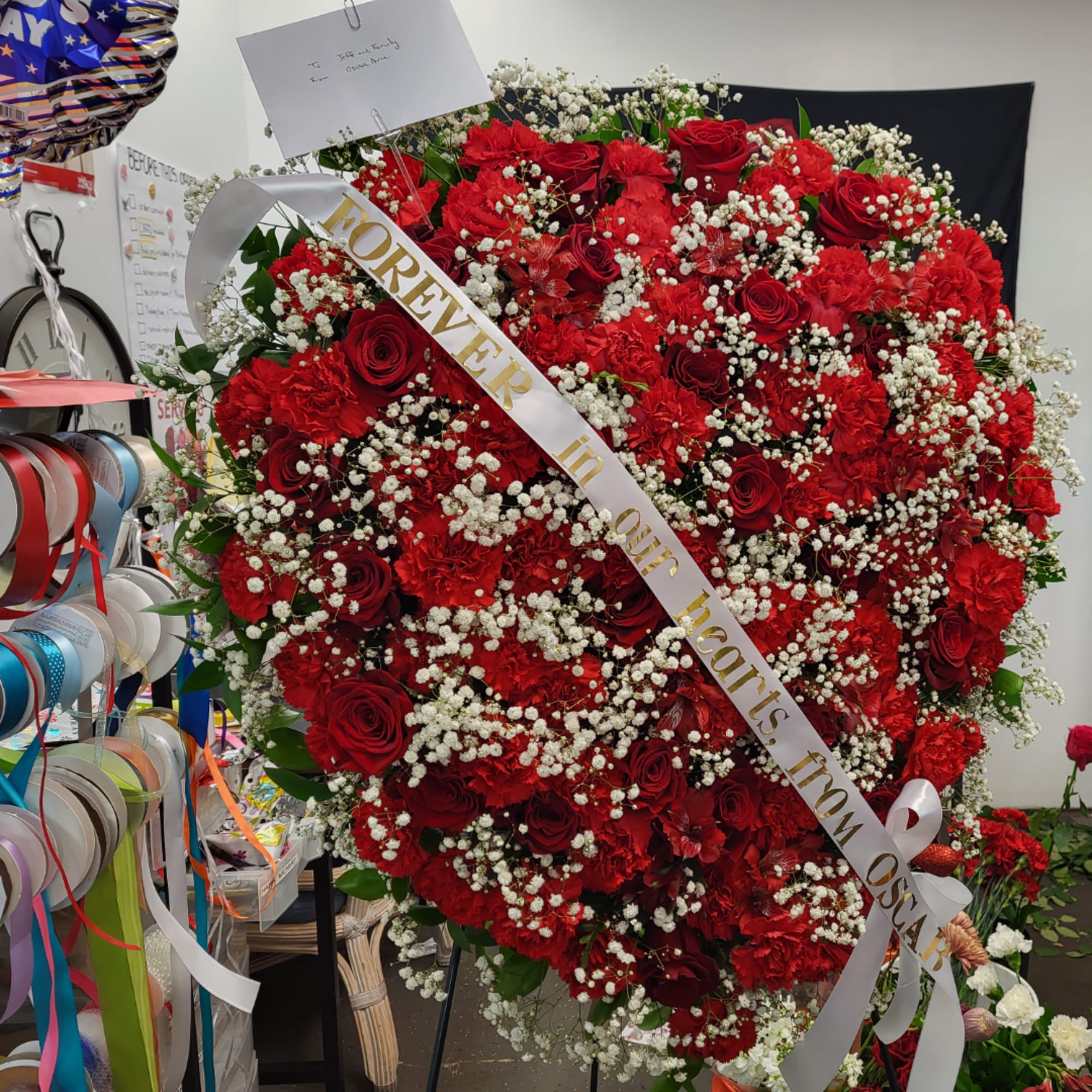 Large heart-shaped red rose and carnation arrangement with white baby's breath and a ribbon