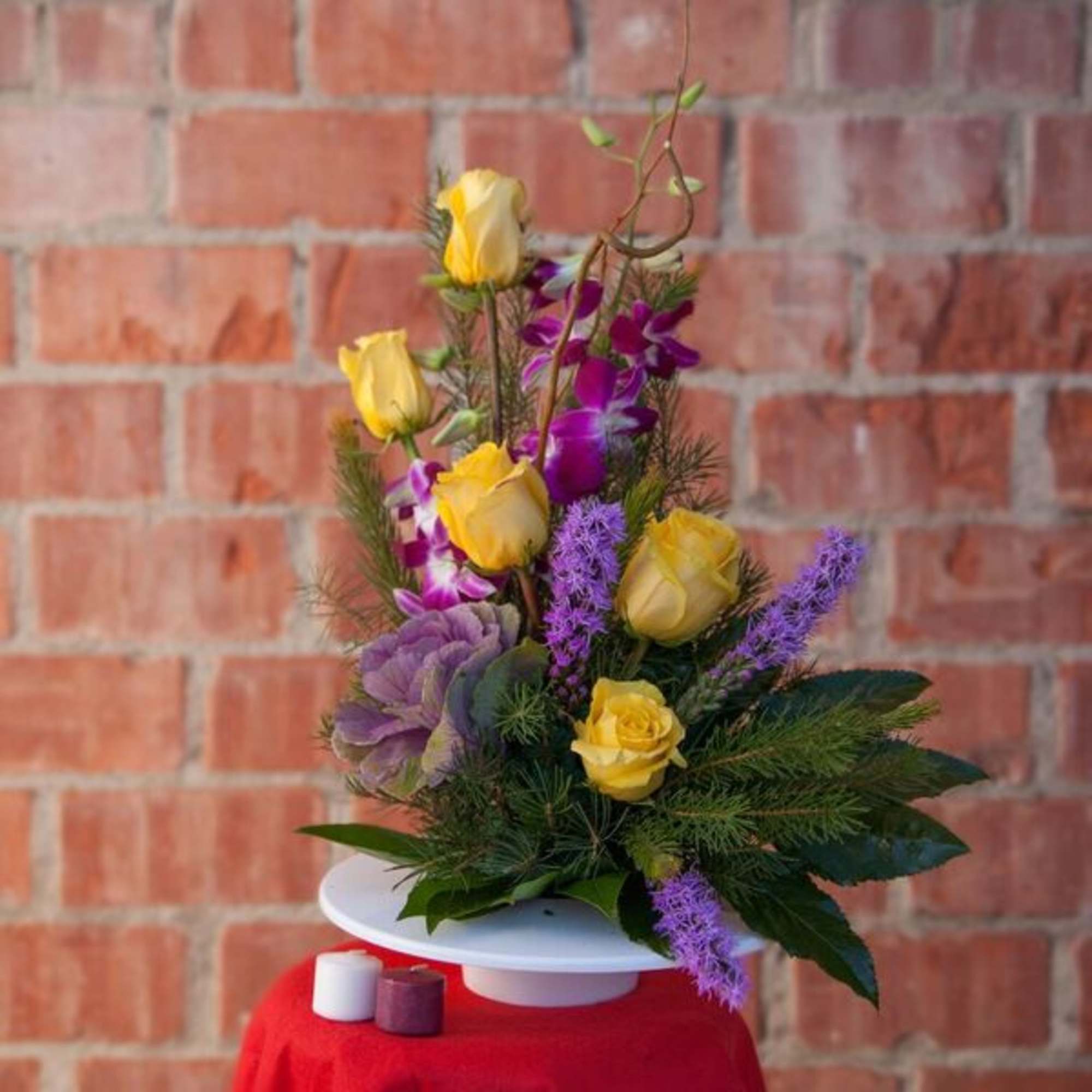 Yellow roses and purple flowers arranged in a white pedestal vase