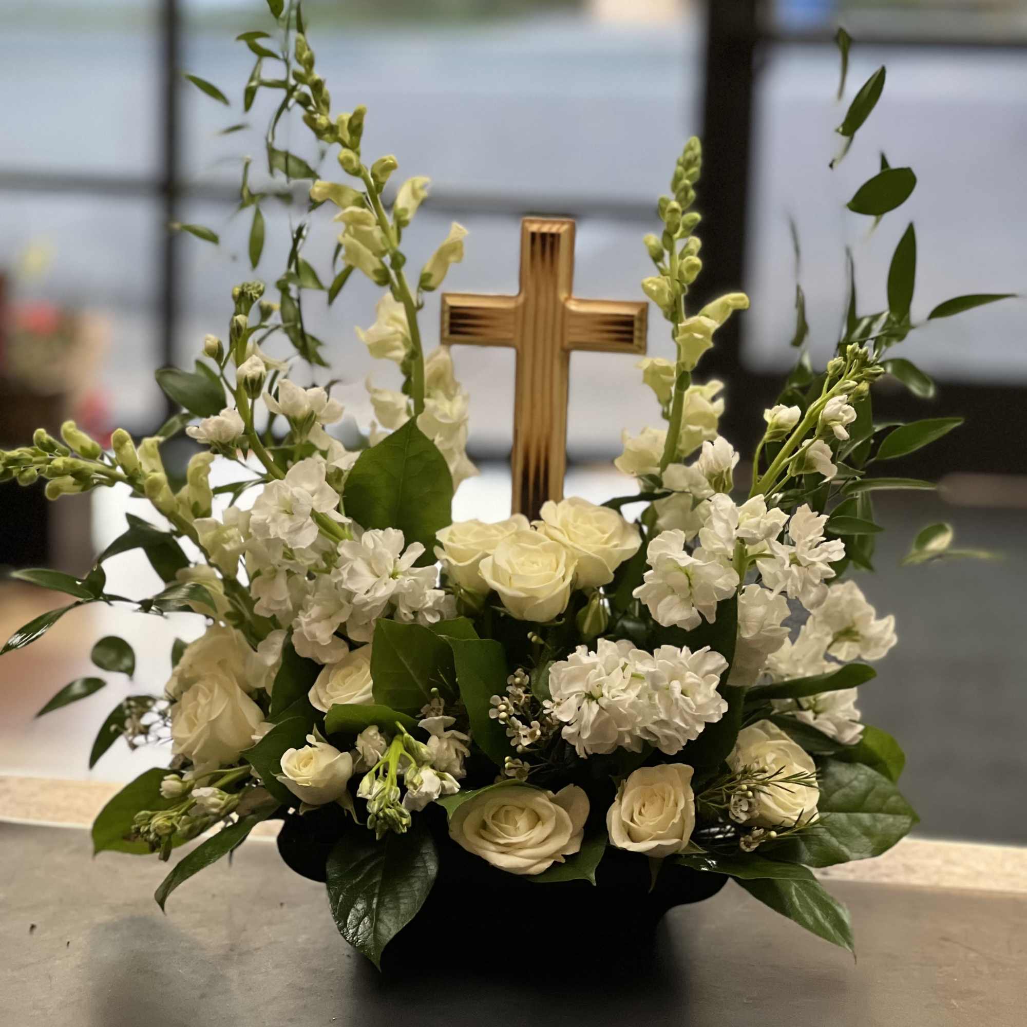 White roses and snapdragons arranged around a wooden cross