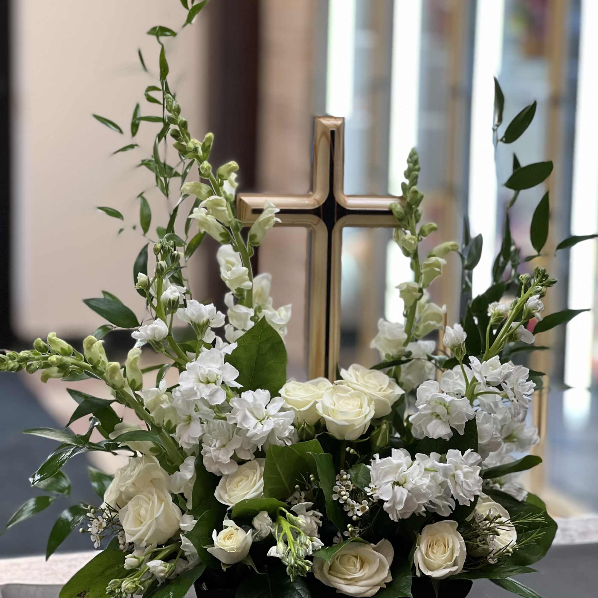 White roses and snapdragons arranged around a gold cross