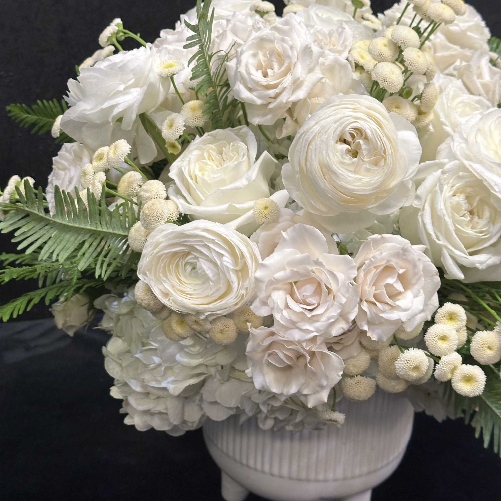 White rose and ranunculus arrangement in a white pedestal vase