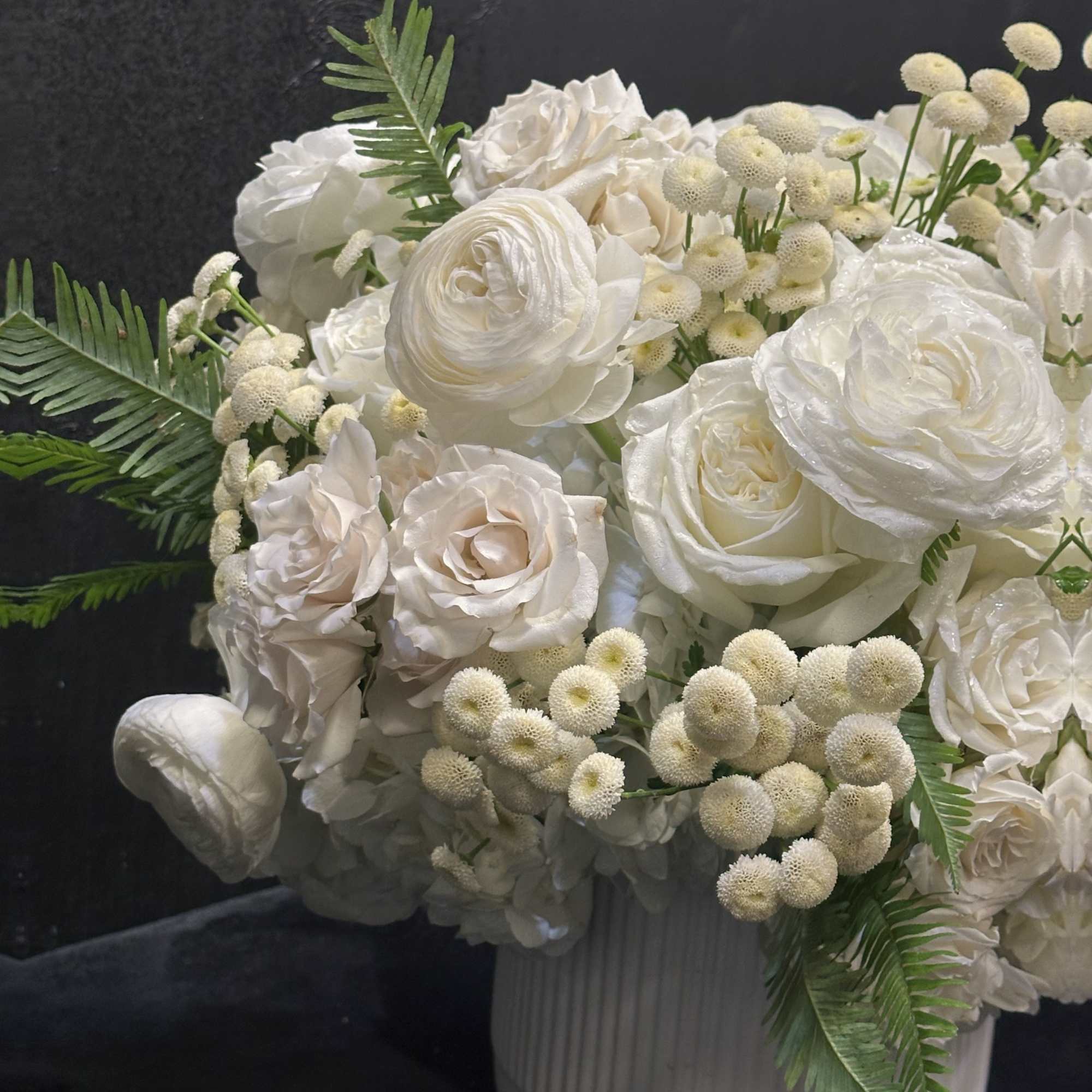 White roses and ranunculus arranged in a white vase.