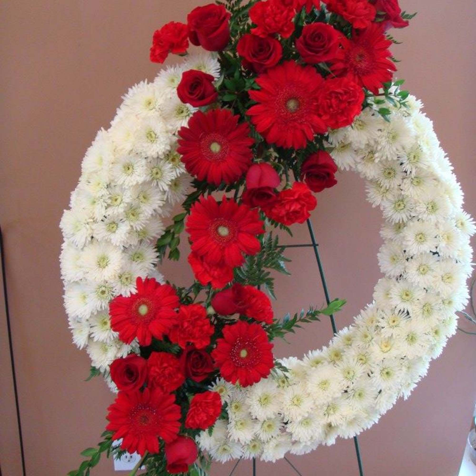 Red and white funeral wreath with roses and daisies on a stand