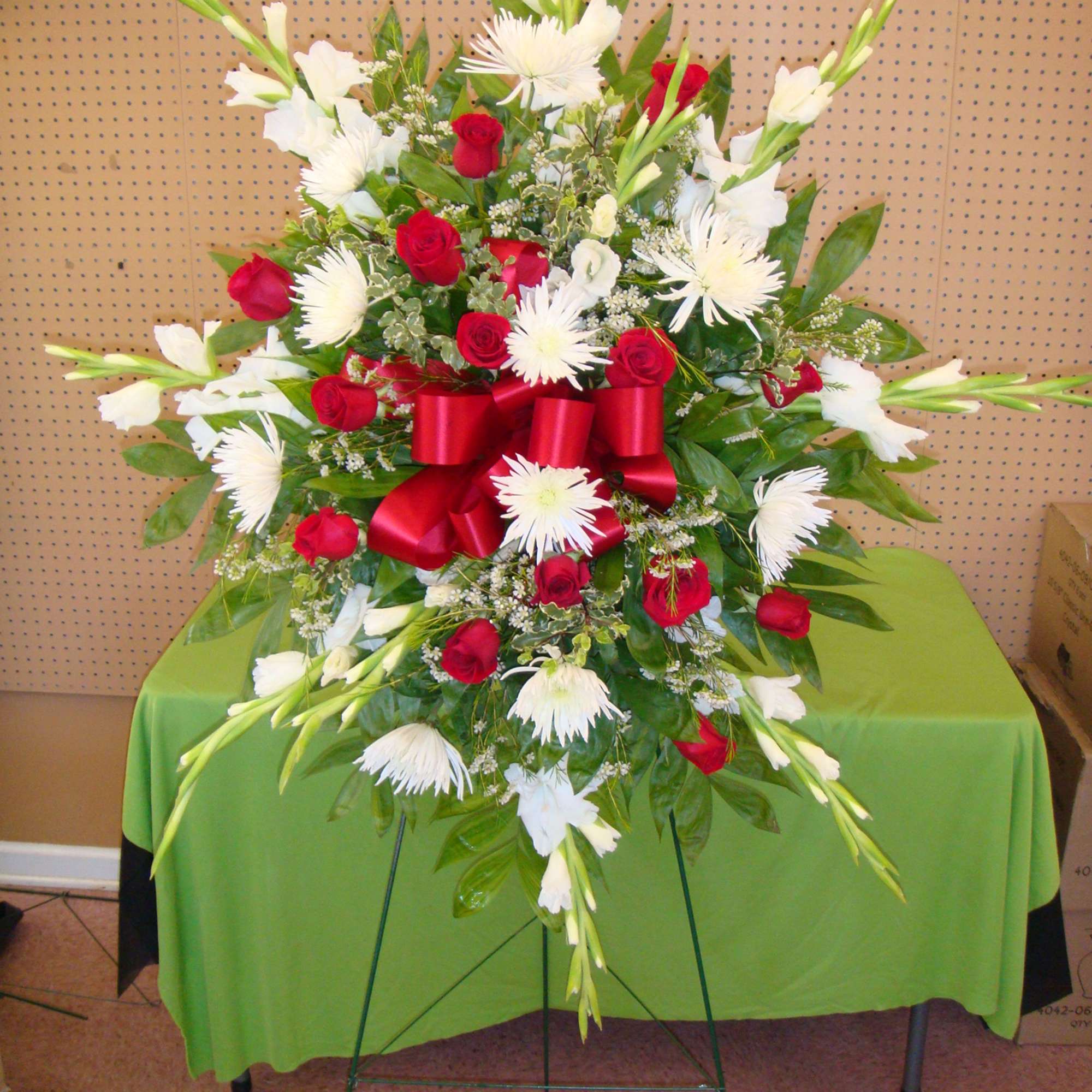 Standing floral spray with red roses and white lilies, accented by a red ribbon