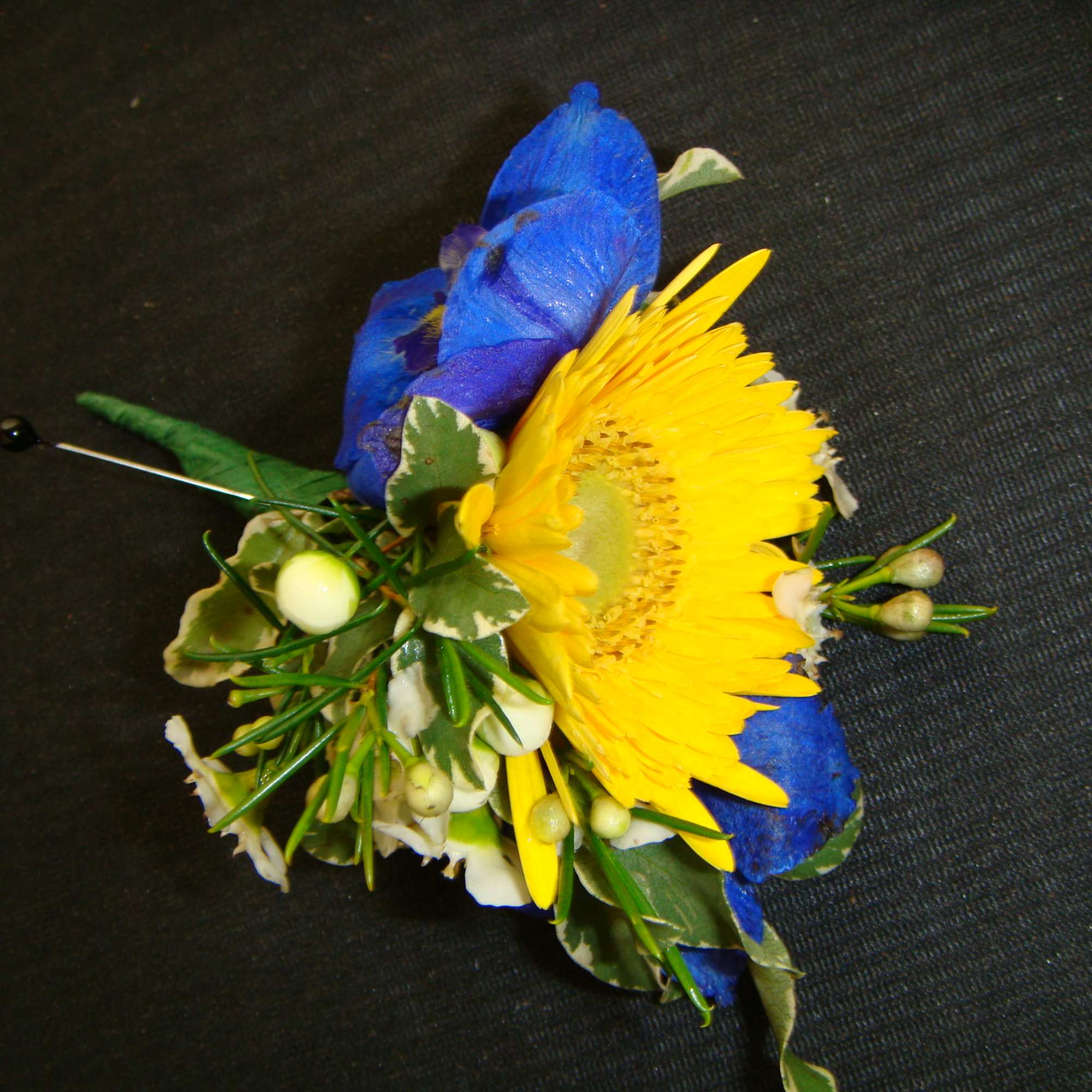 Blue and yellow floral boutonniere with berries and greenery