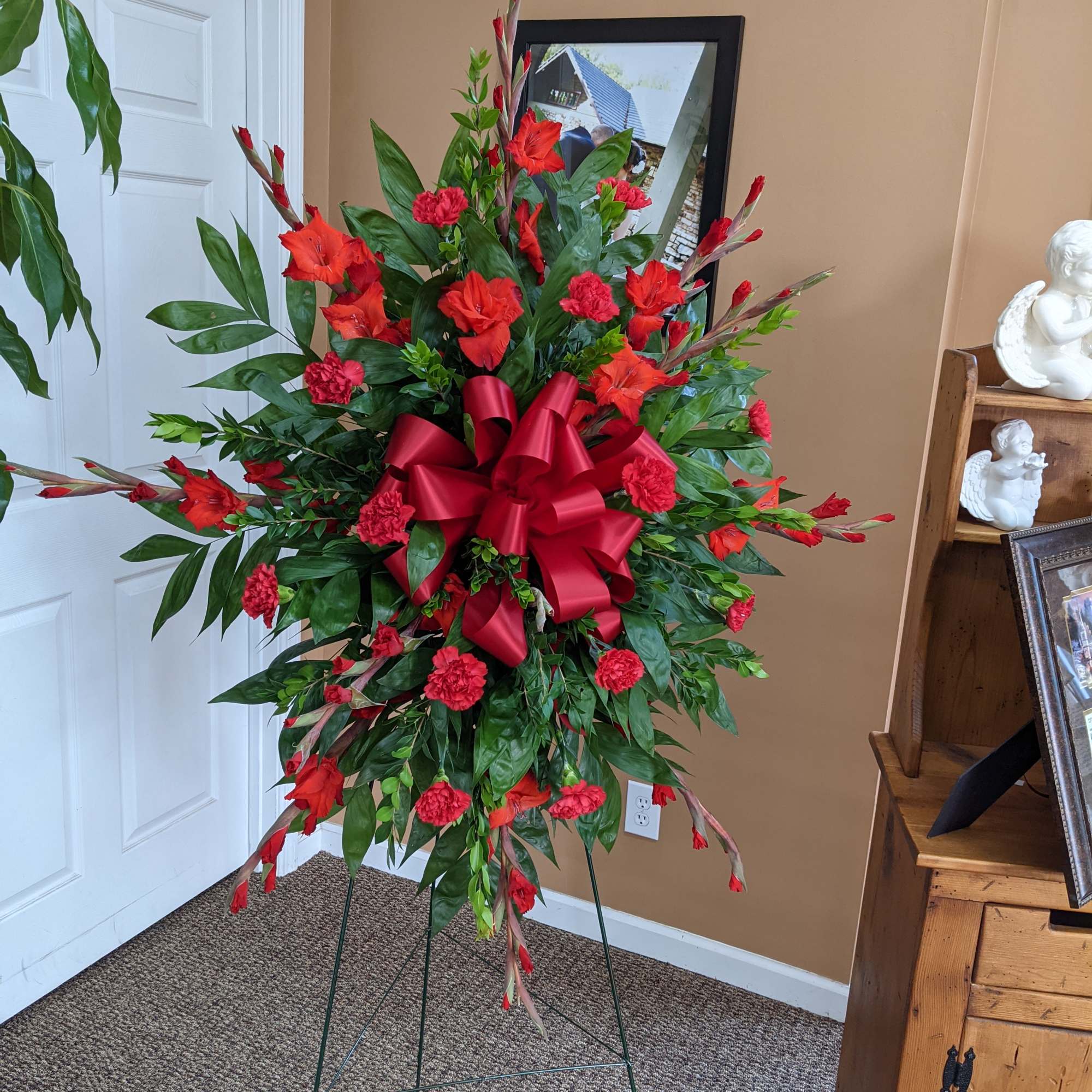 Tall red floral standing spray with a large ribbon bow