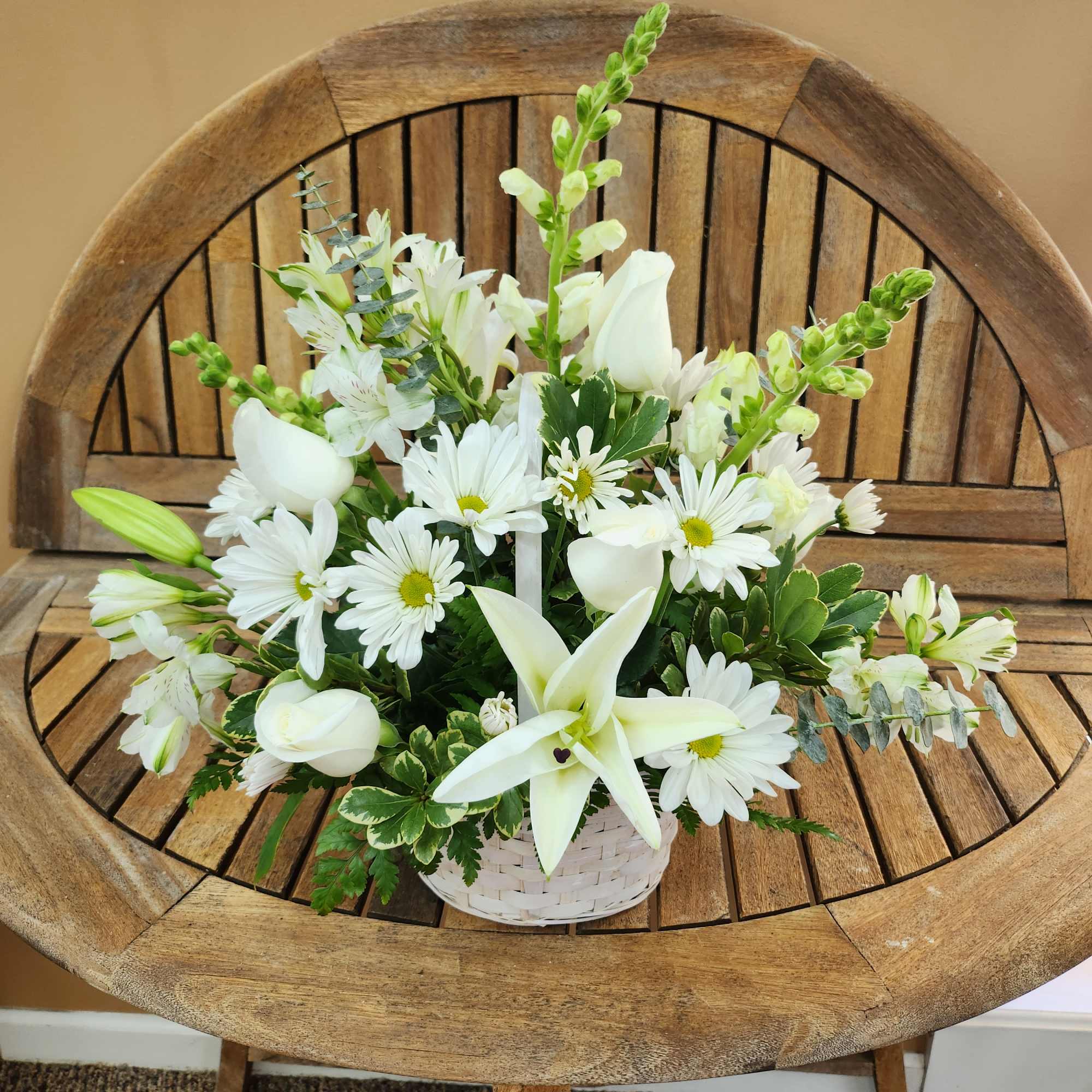 White floral arrangement in a white basket with daisies and lilies