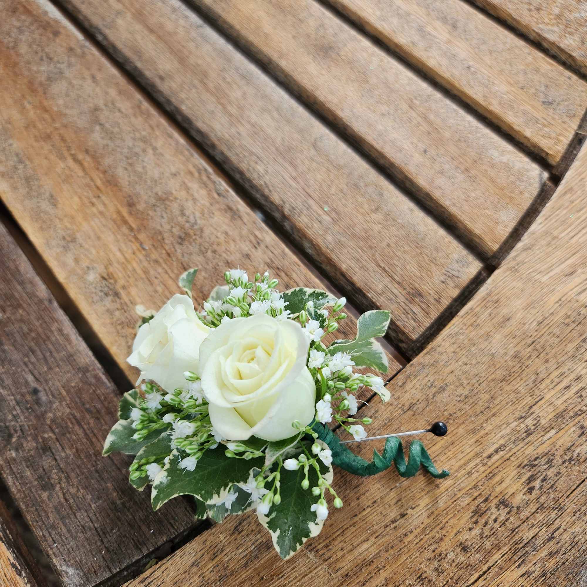 White rose boutonniere with small white filler flowers and variegated greenery