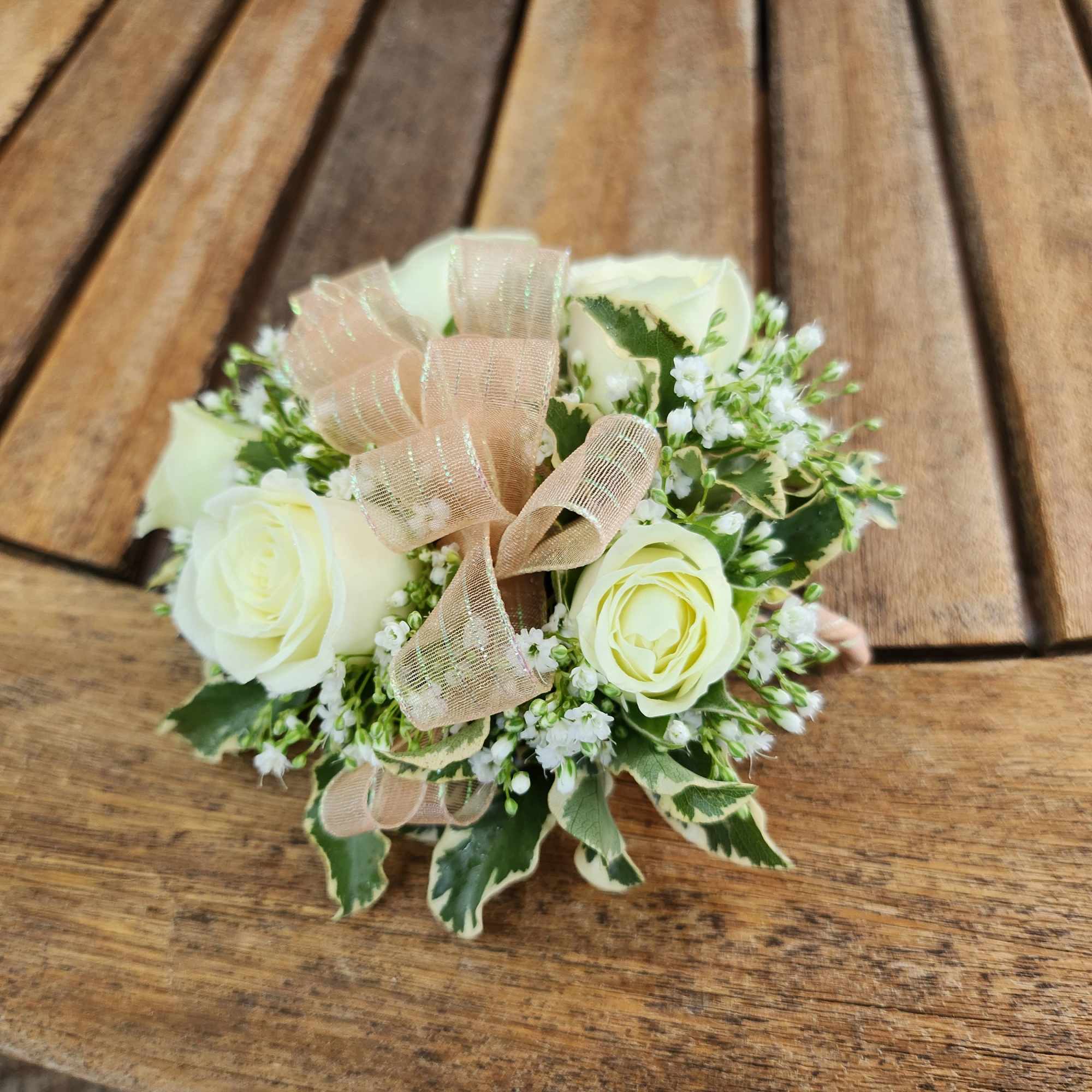 Small bouquet of white roses with a beige ribbon on a wooden table