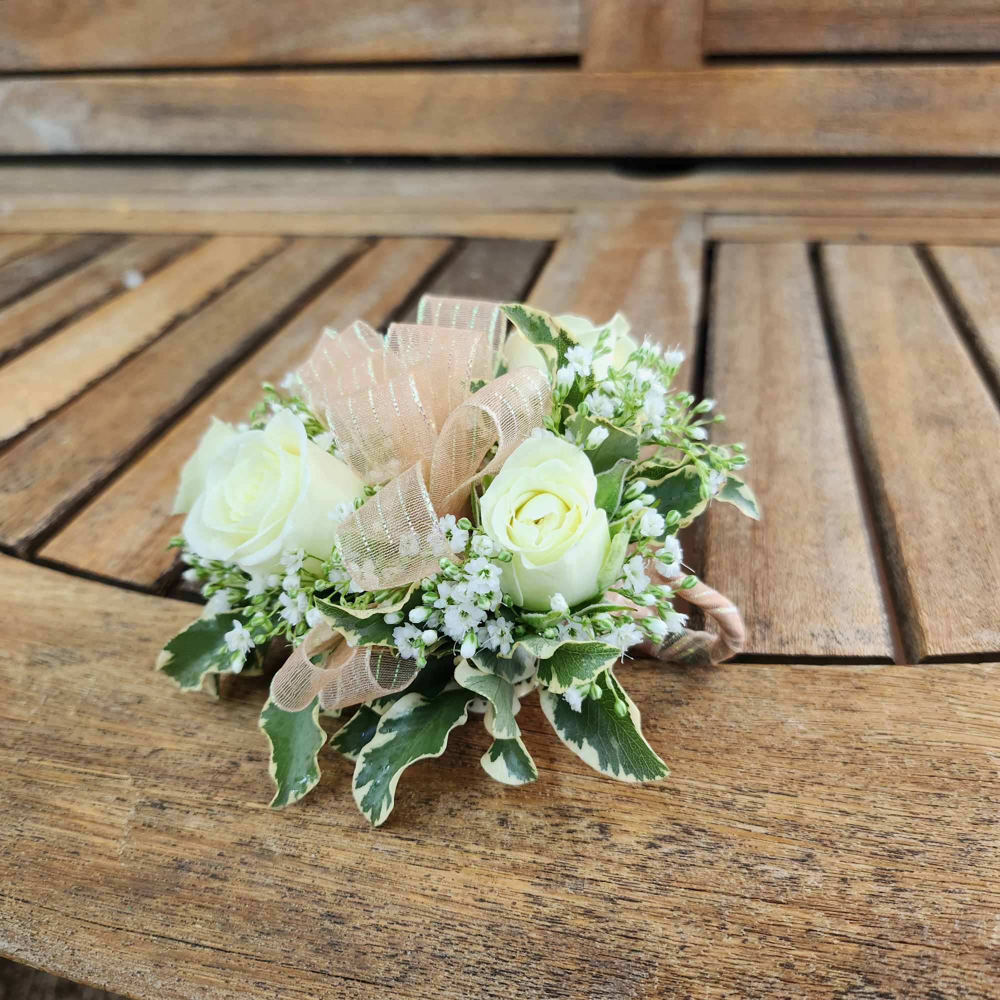Small white rose arrangement with ribbon on a wooden bench