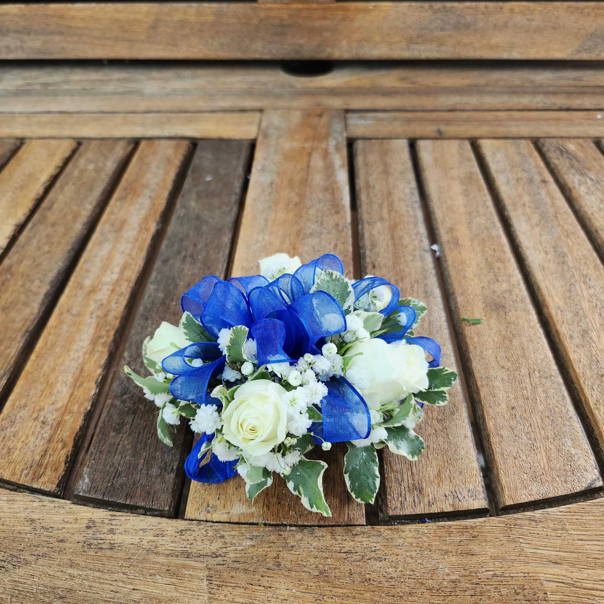 Small white rose arrangement with blue ribbon on a wooden table