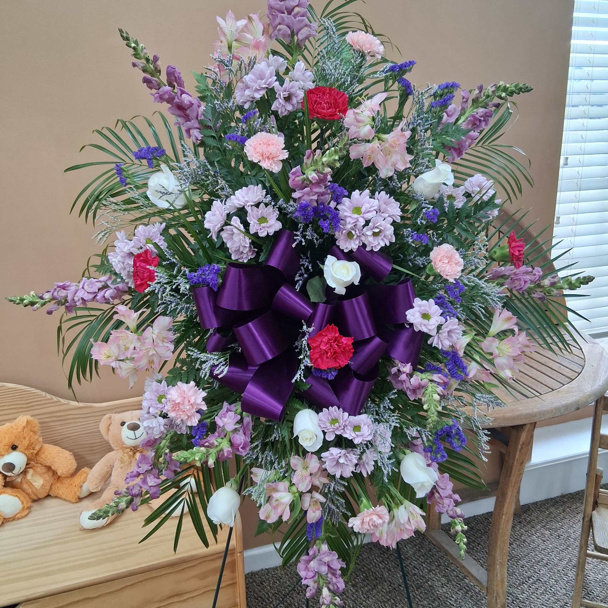 Large standing floral spray with purple ribbon and pastel blooms