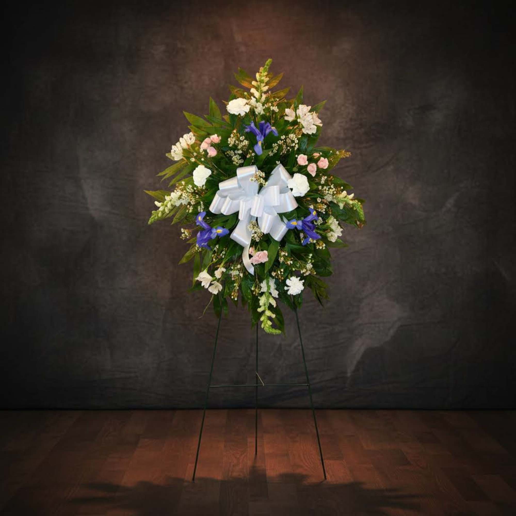 Standing floral wreath with white, pink, and blue flowers and a white bow