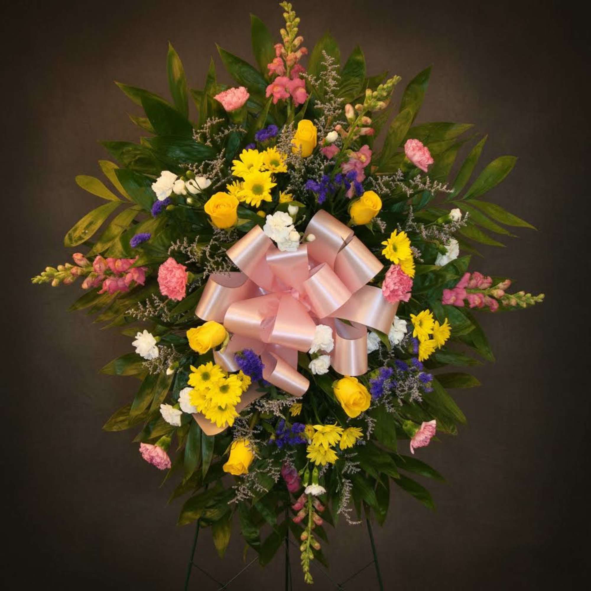 Standing floral spray with yellow, pink, white, and purple flowers and a pink bow