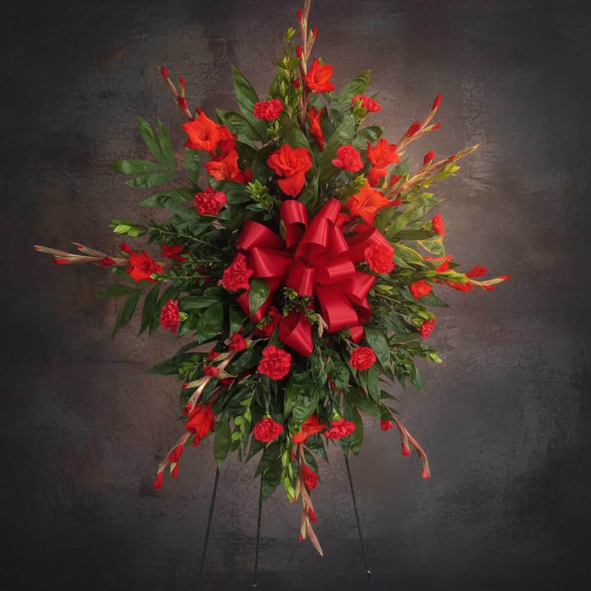 Red floral standing spray with a large ribbon on a black easel