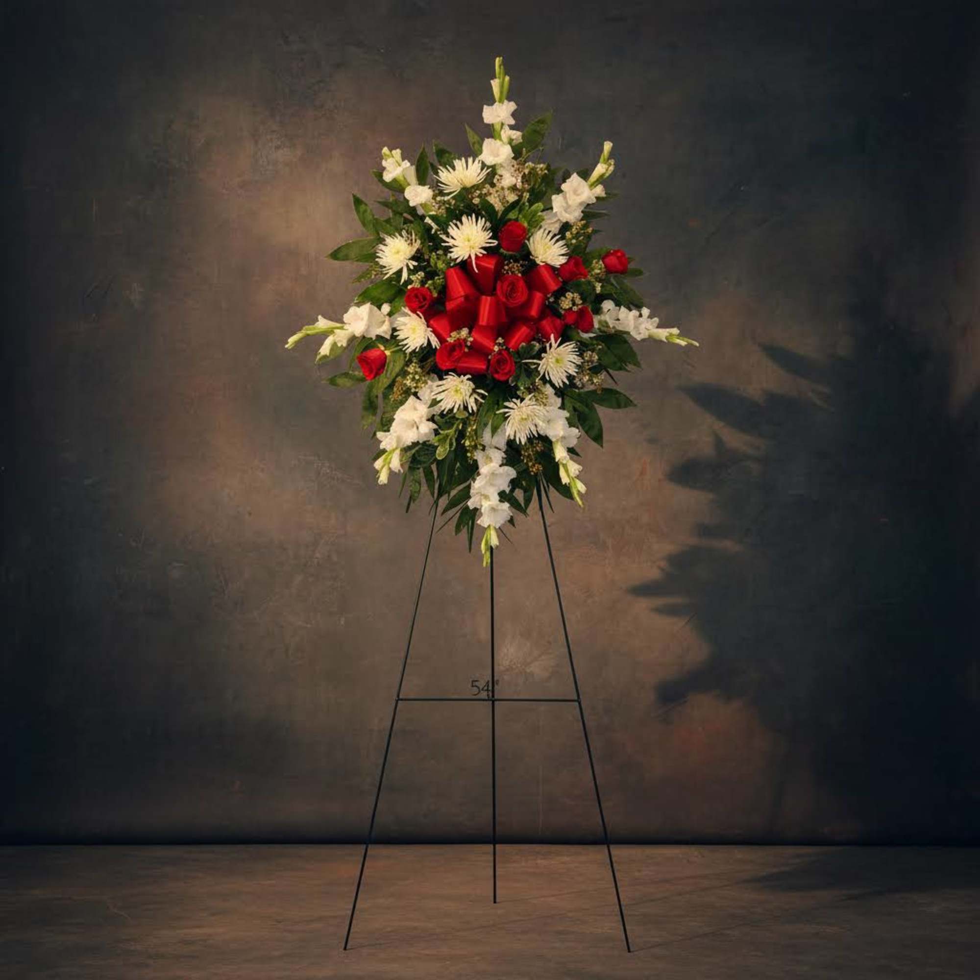 Standing floral spray with red roses and white flowers on a metal easel