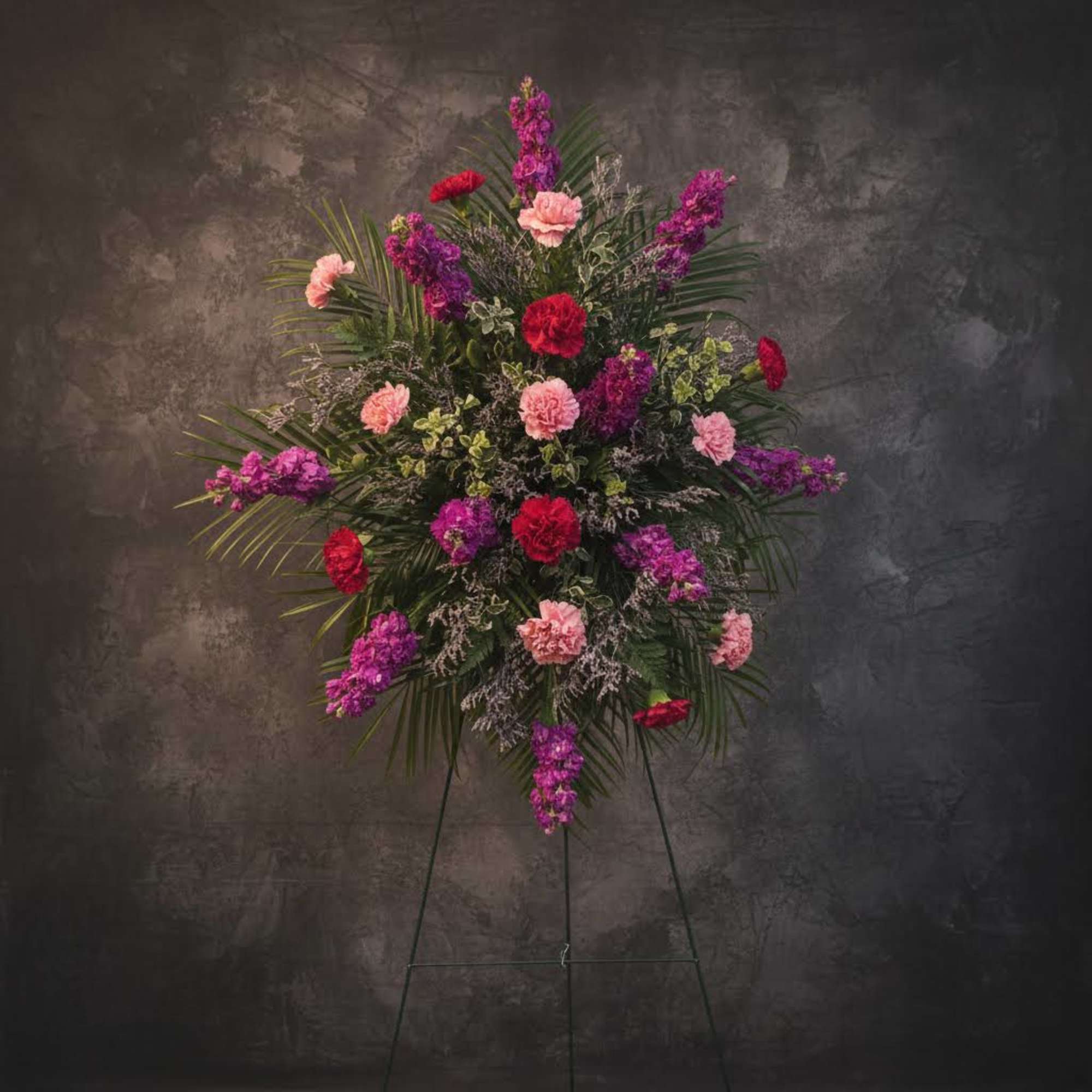Standing floral spray with pink, purple, and red carnations on an easel