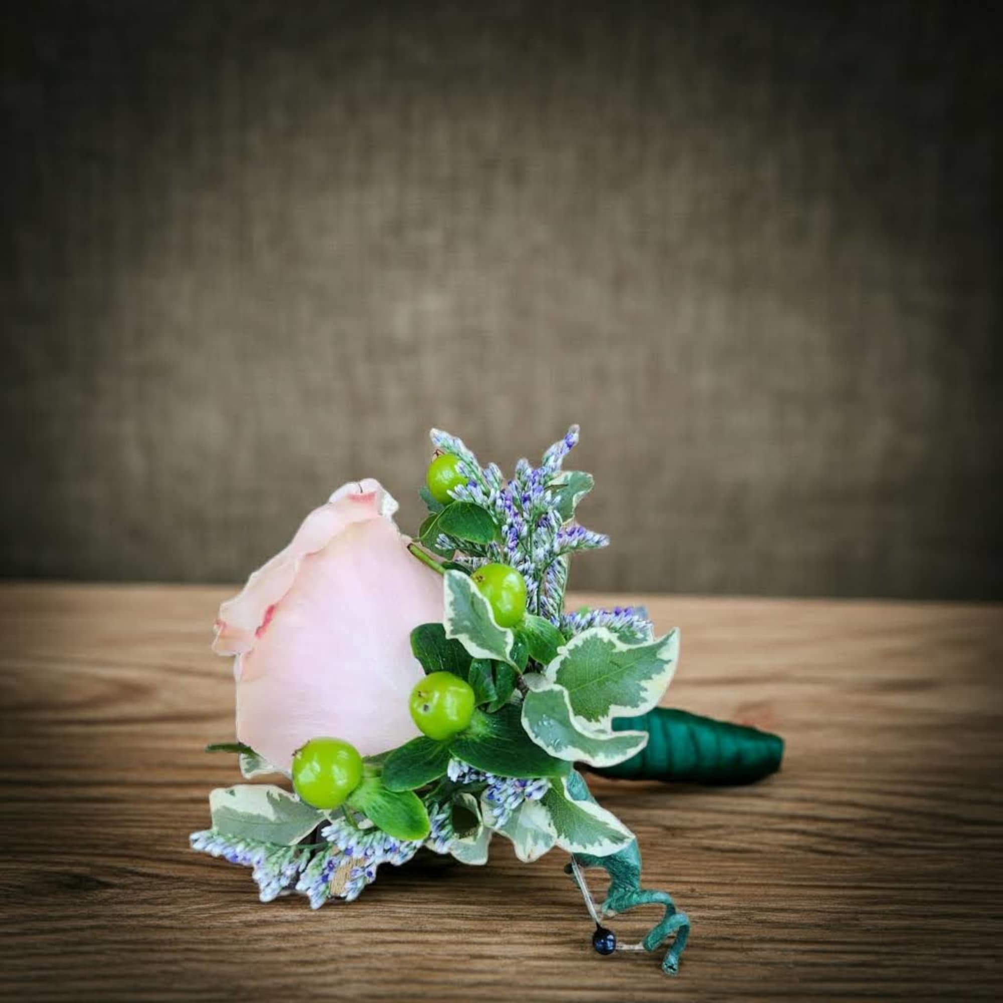 Pink rose boutonniere with green berries and purple filler flowers