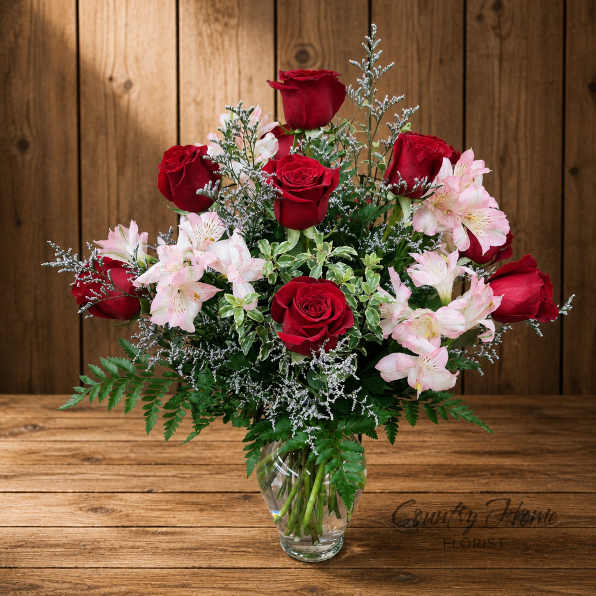 Red roses and pale pink flowers arranged in a clear glass vase