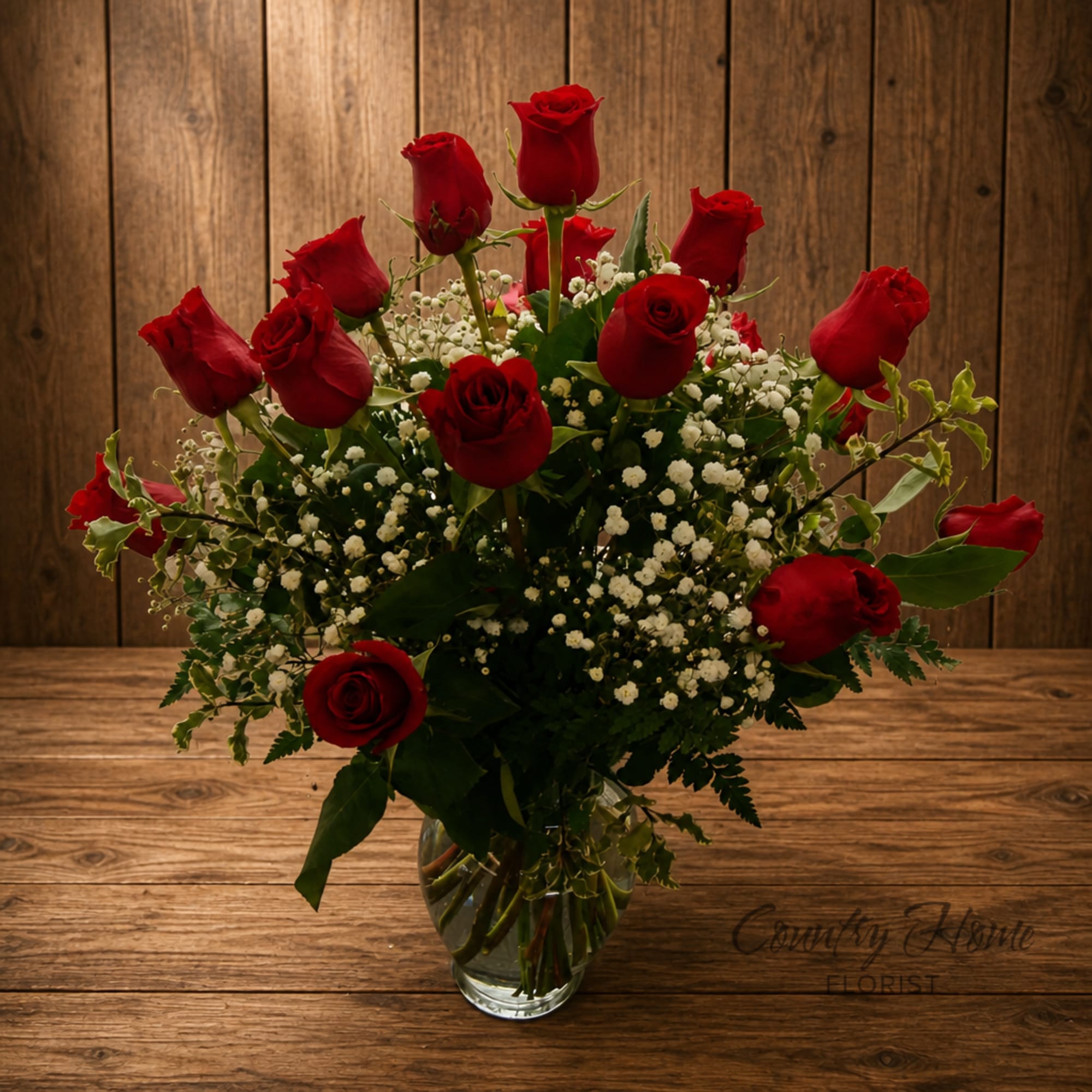 Red roses arranged in a clear glass vase with white filler flowers