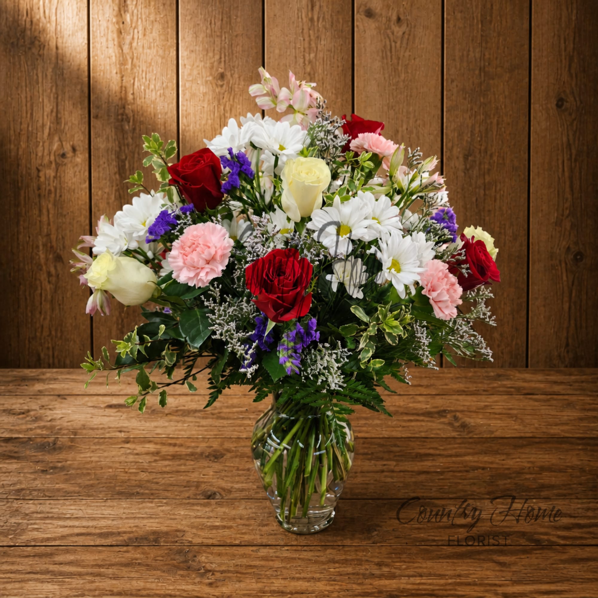Mixed bouquet of roses, daisies, and carnations in a clear glass vase