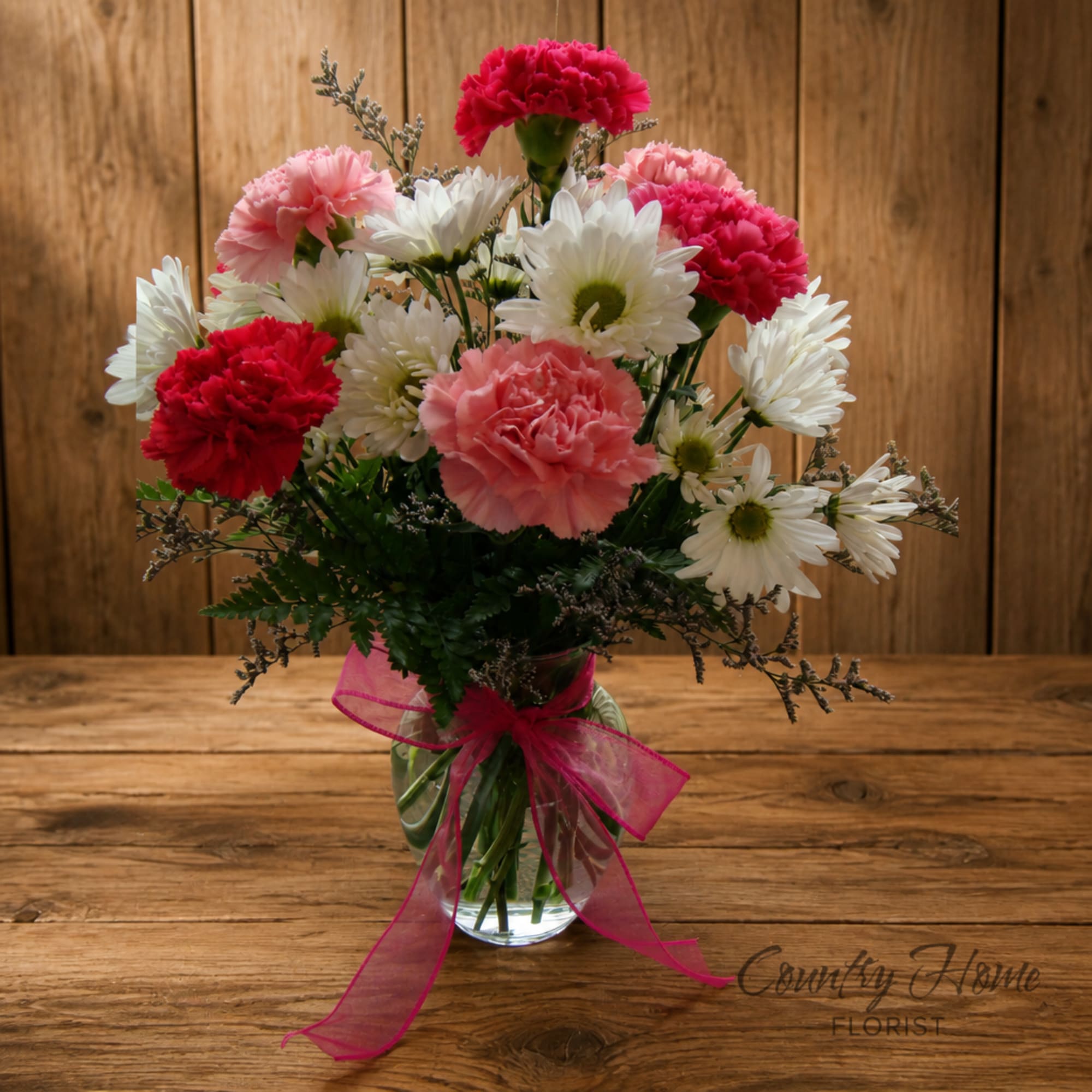 Pink and white carnations with daisies in a glass vase tied with a pink ribbon