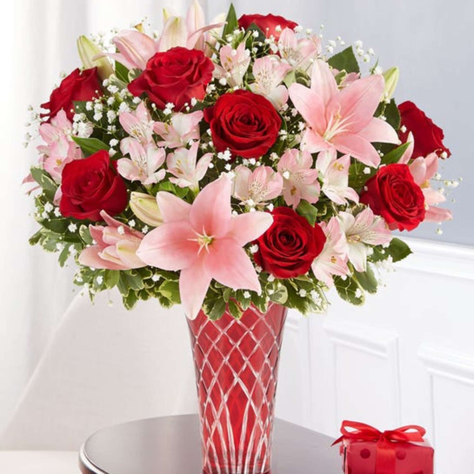 Bouquet of red roses and pink lilies in a red glass vase