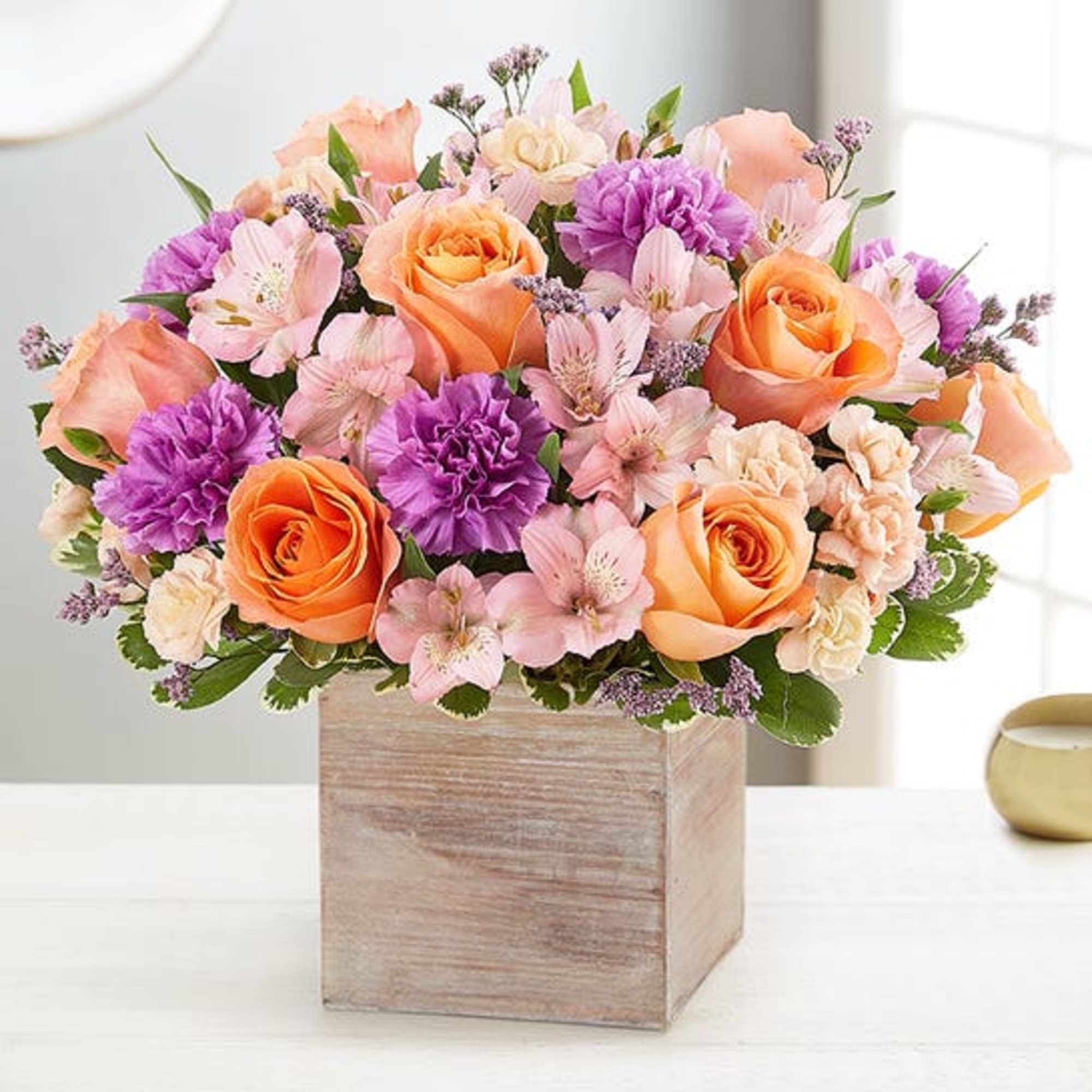 Mixed bouquet of orange roses, pink flowers, and purple blooms in a wooden box