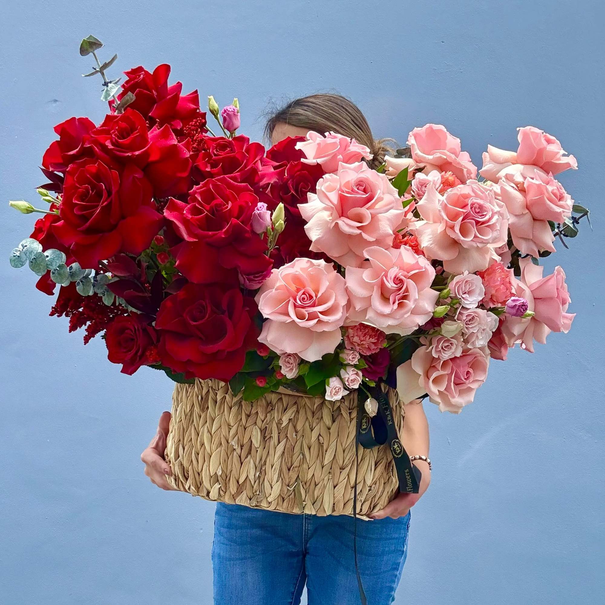 Large basket arrangement of red and pink roses held by a person