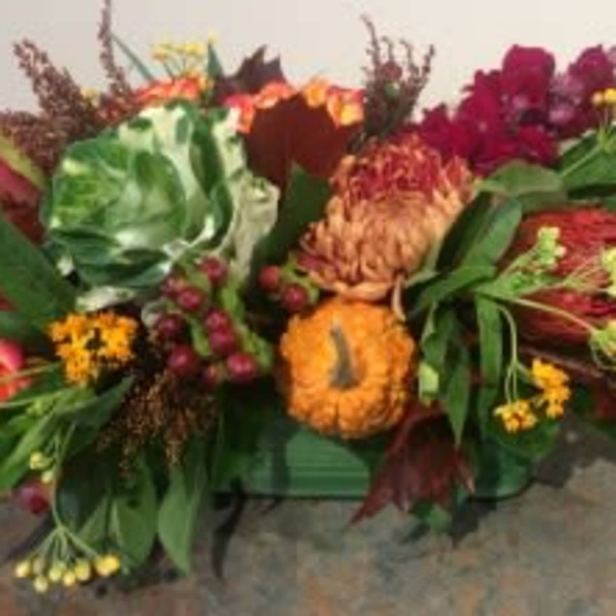 Low autumn centerpiece with orange and burgundy flowers, mini calla lilies, cabbage, and small gourds in a green container
