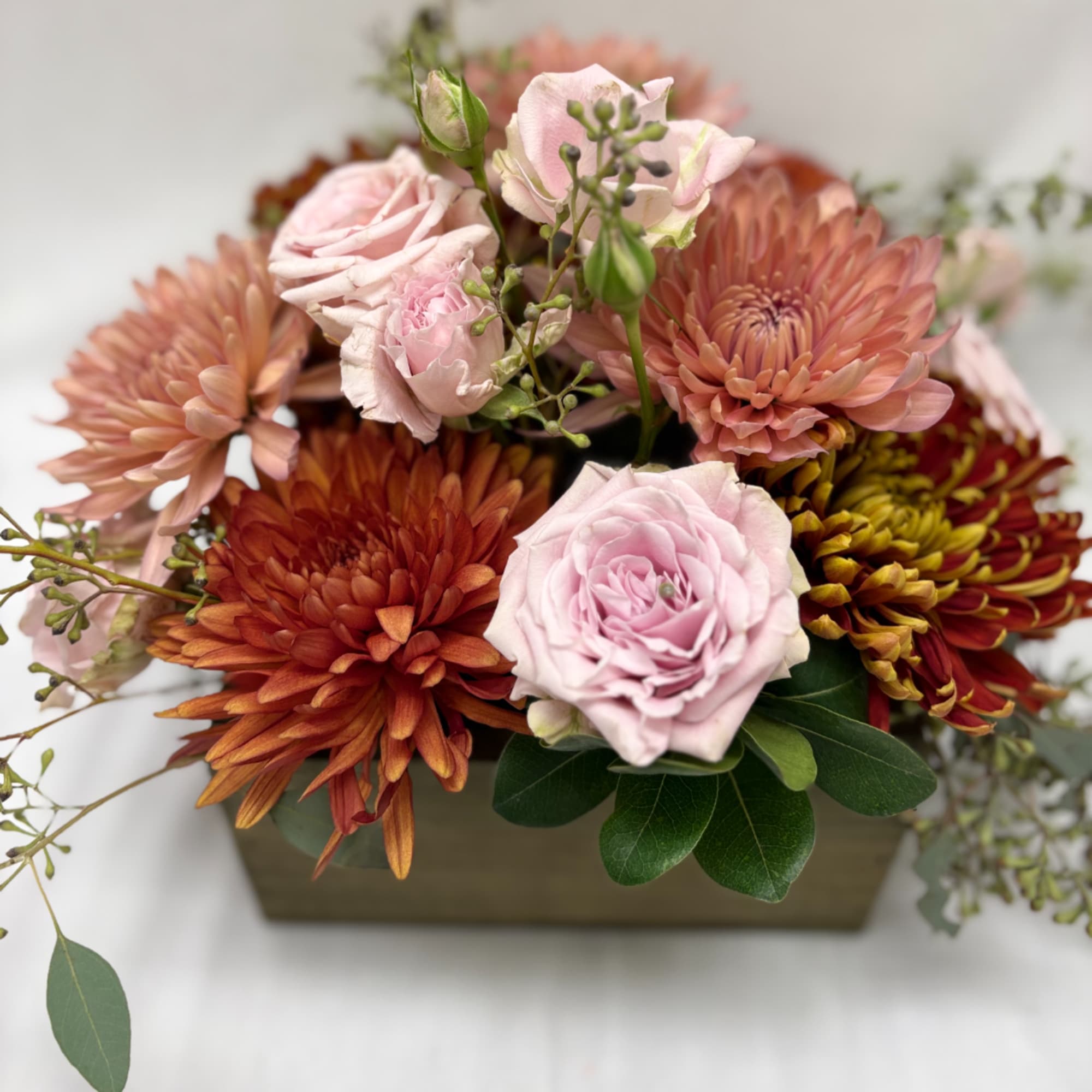 Pink roses and orange chrysanthemums arranged in a rectangular vase