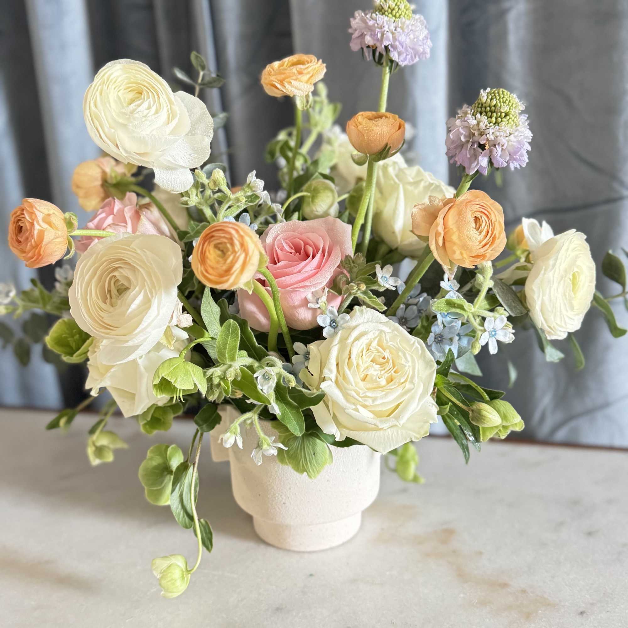 Pastel bouquet of roses and ranunculus in a white vase