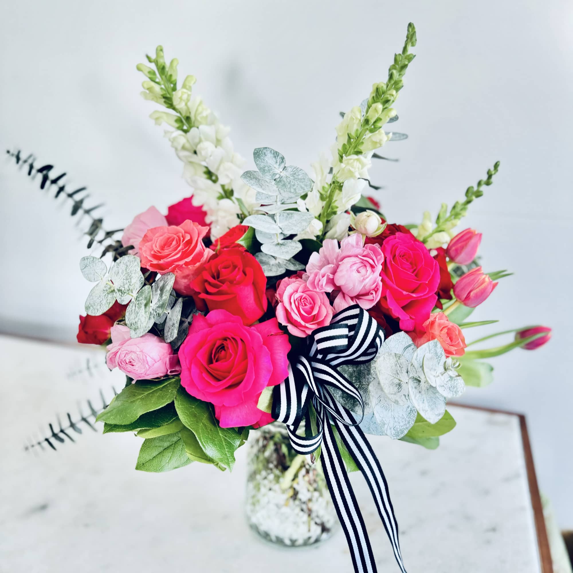 Bouquet of pink and red roses with white snapdragons in a glass vase