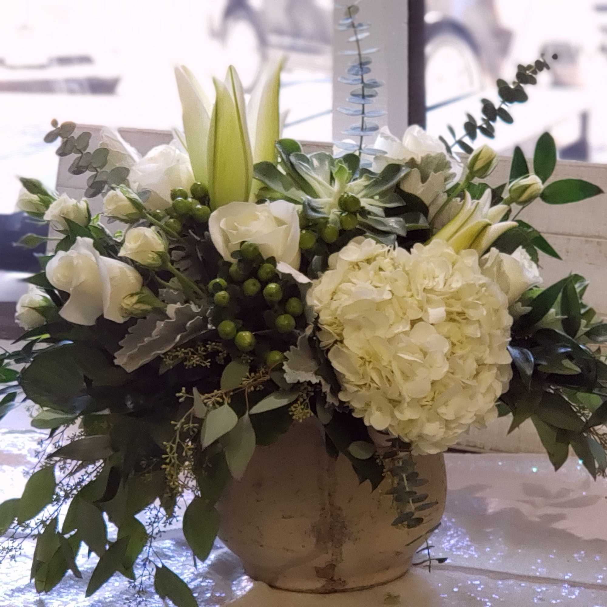 White floral arrangement in a rustic vase with lilies and hydrangea