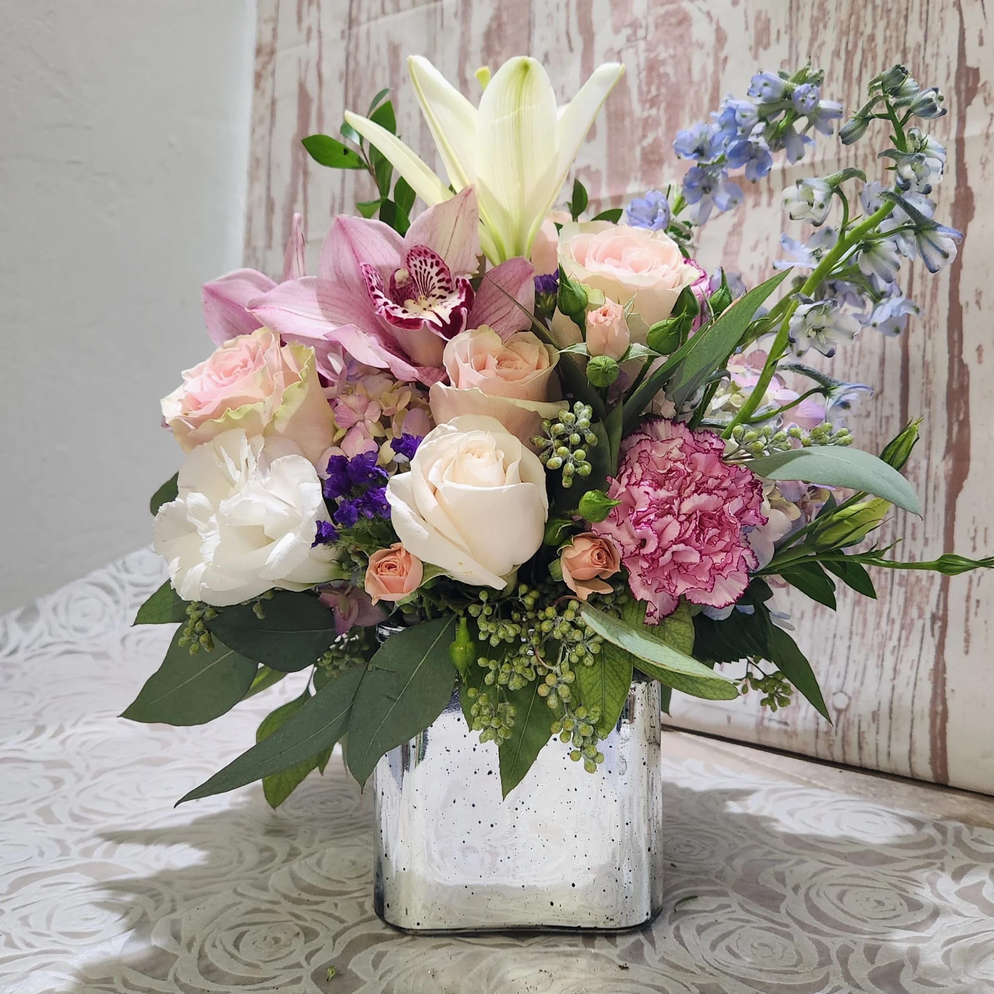 Mixed bouquet in a square glass vase with roses, lilies, and blue flowers