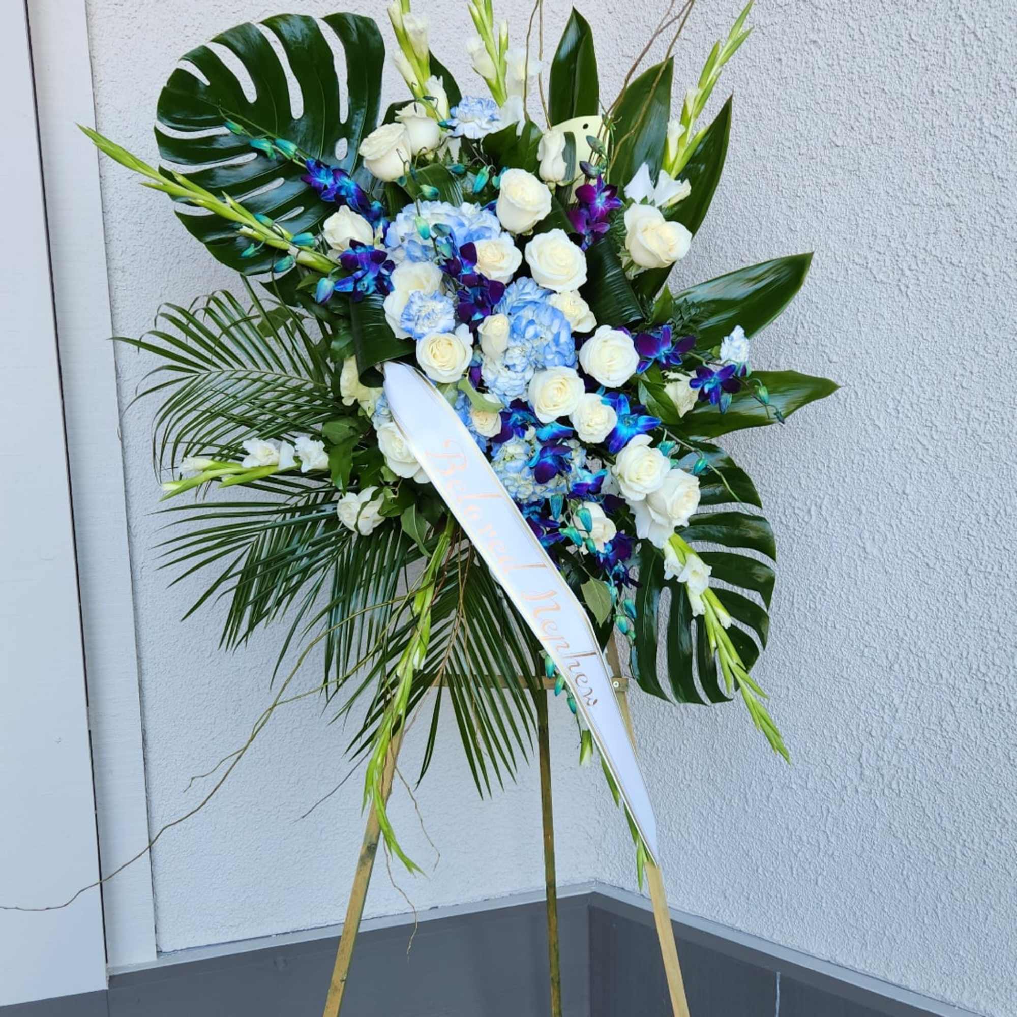 Tall standing floral spray with white roses, blue hydrangeas, and purple orchids