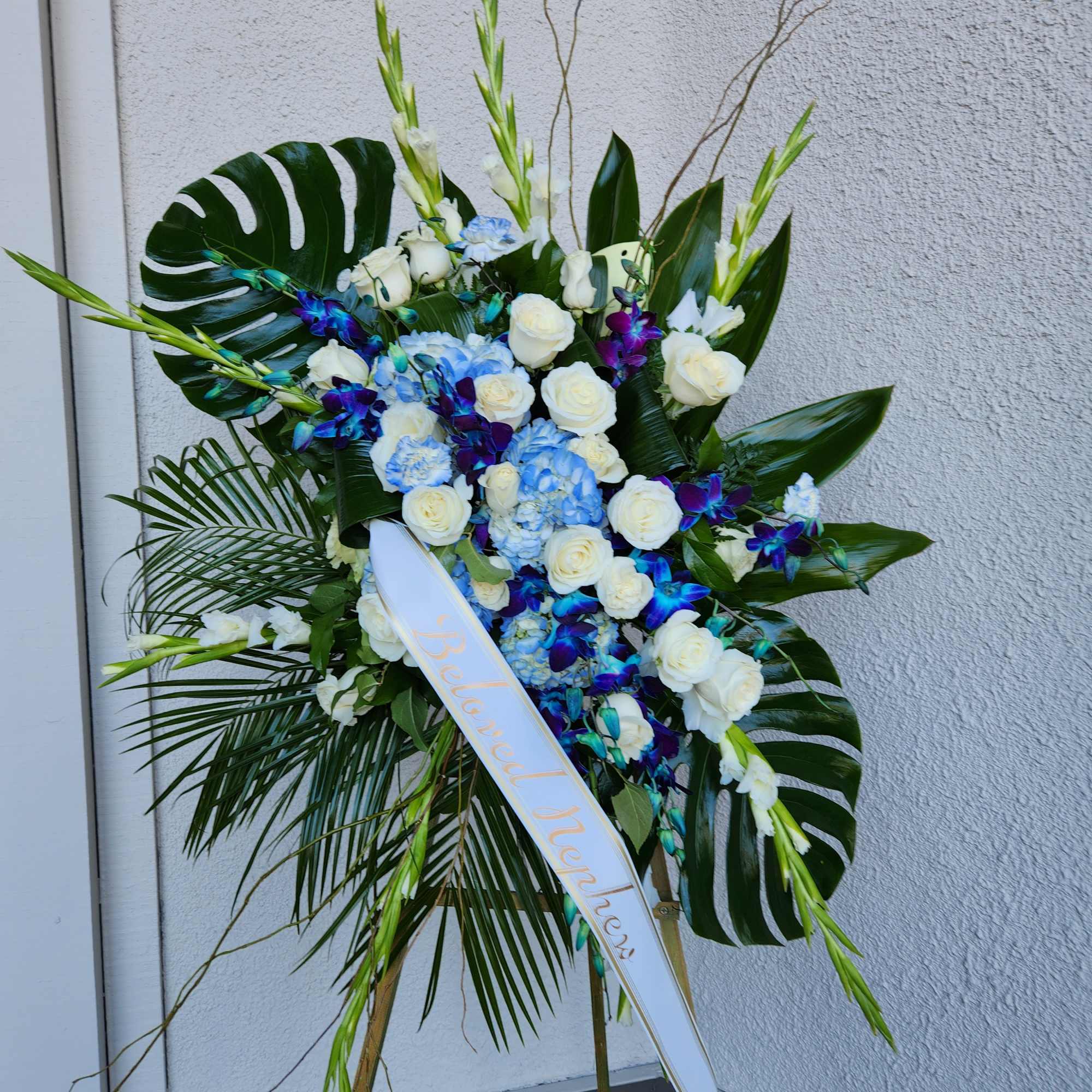 Standing floral spray with white roses, blue hydrangeas, and purple orchids