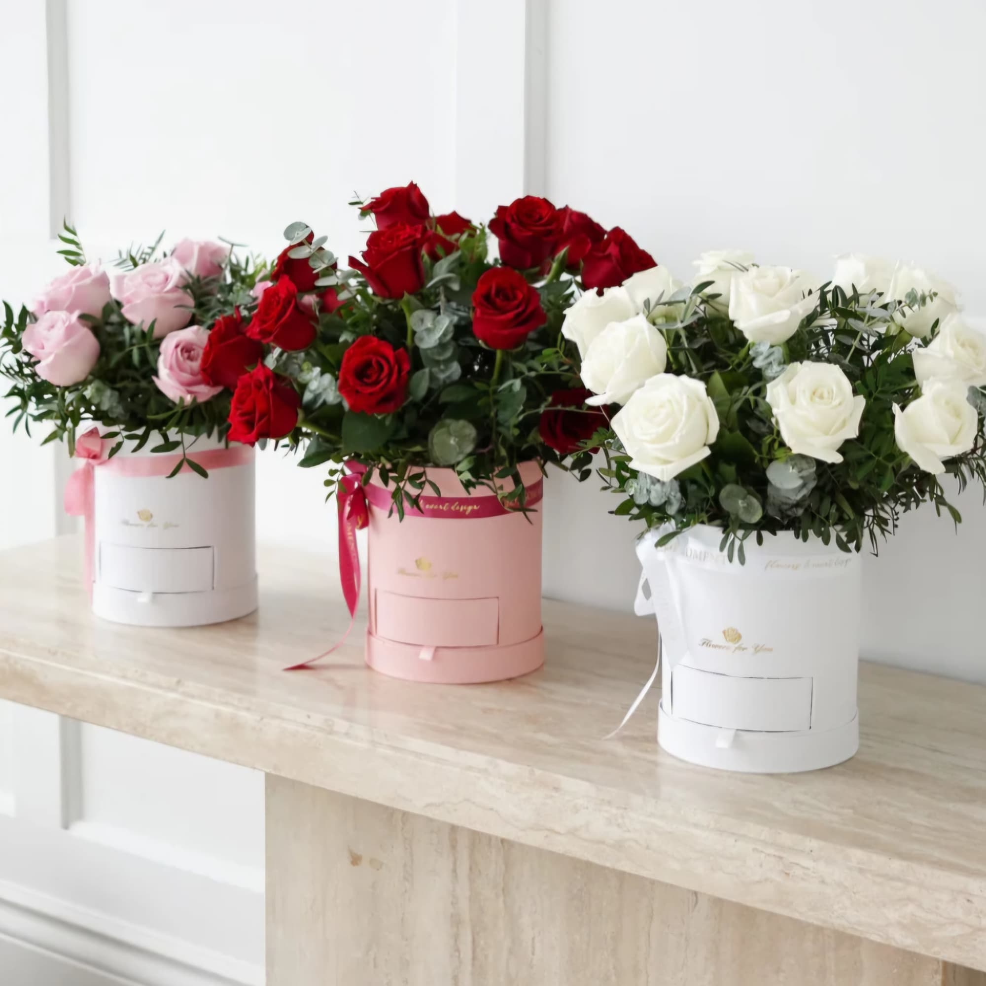 Three rose arrangements in pink, red, and white hat boxes