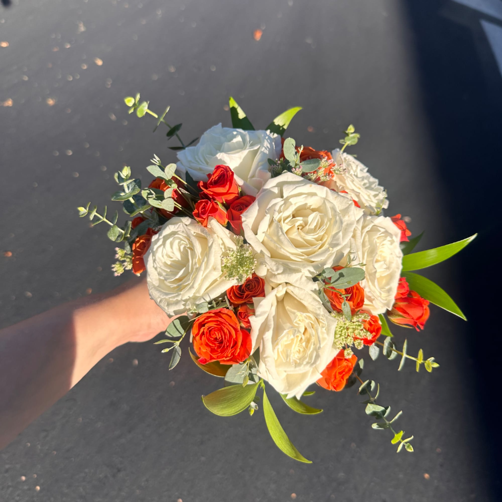 Handheld bouquet of white and red roses with greenery