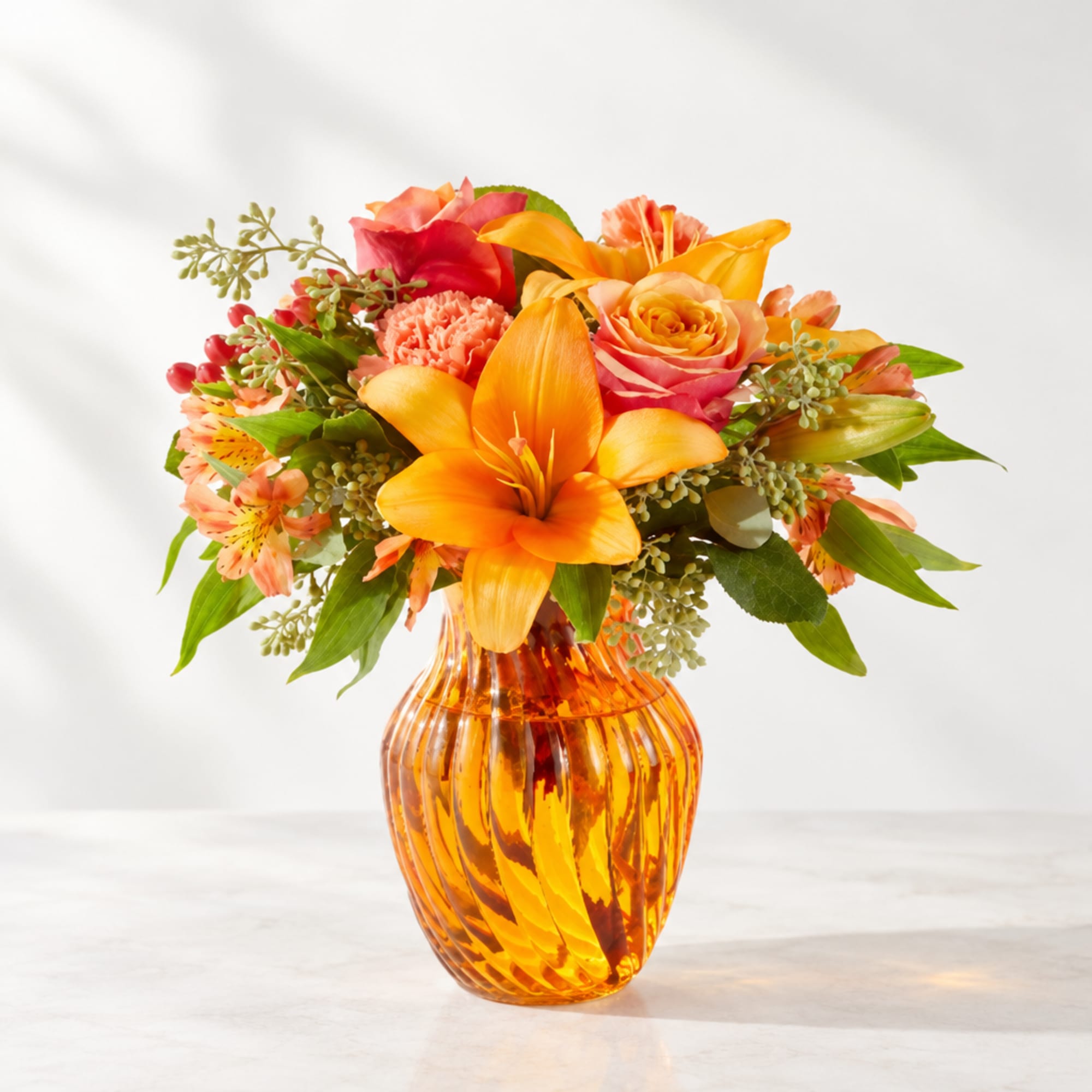 Orange and pink mixed bouquet in an amber glass vase