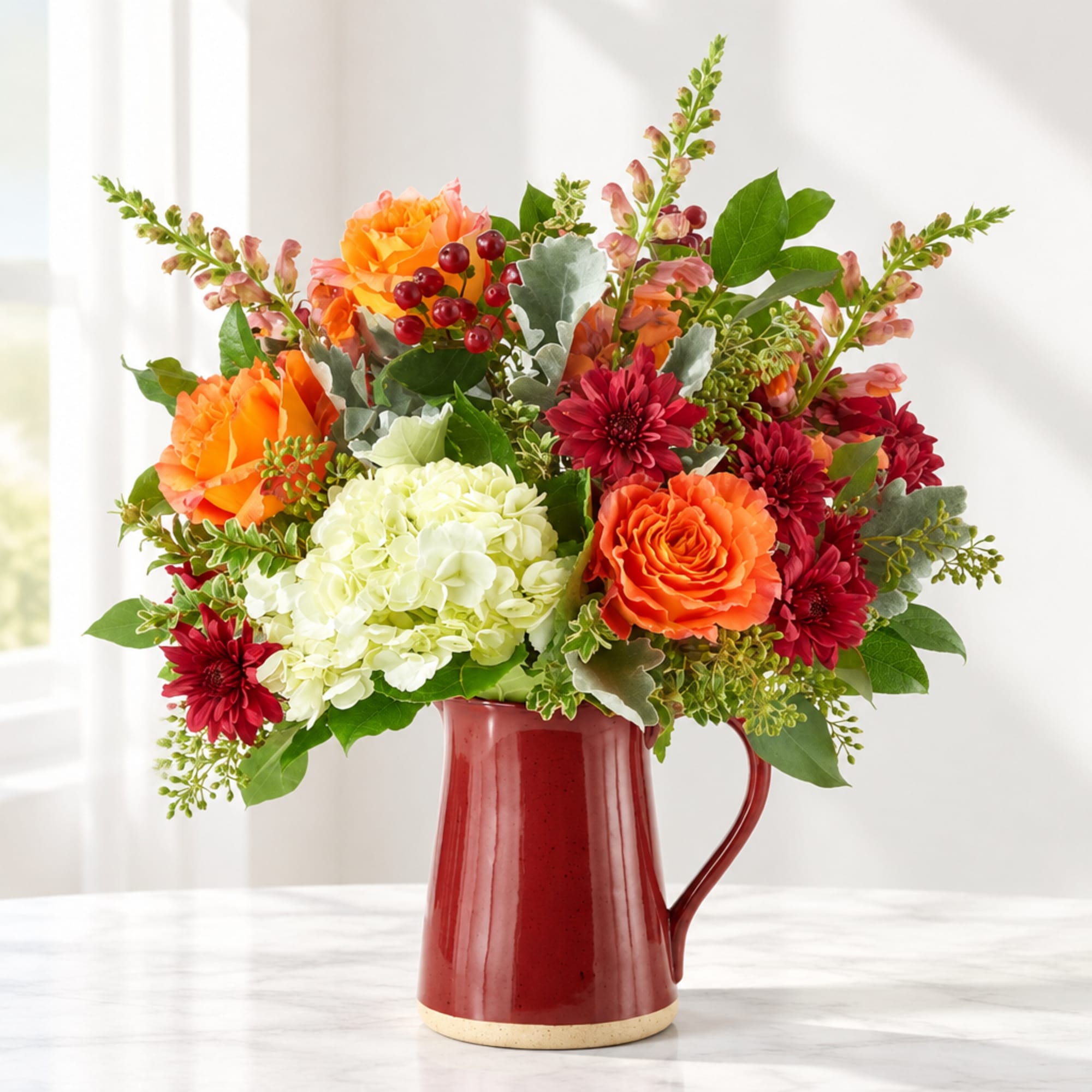 Orange and red mixed flowers arranged in a red pitcher vase