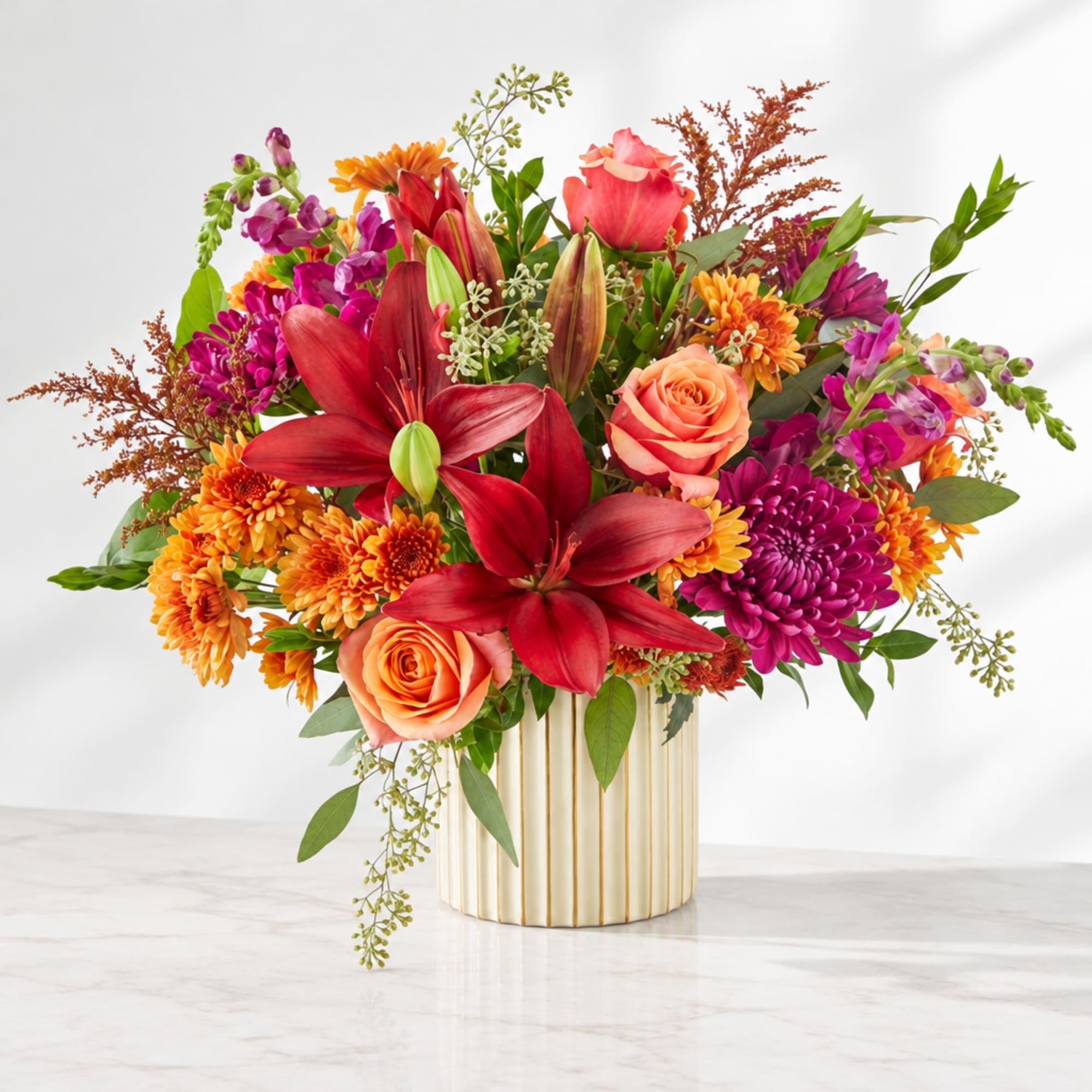 Colorful mixed bouquet in a striped gold vase with red lilies and orange roses